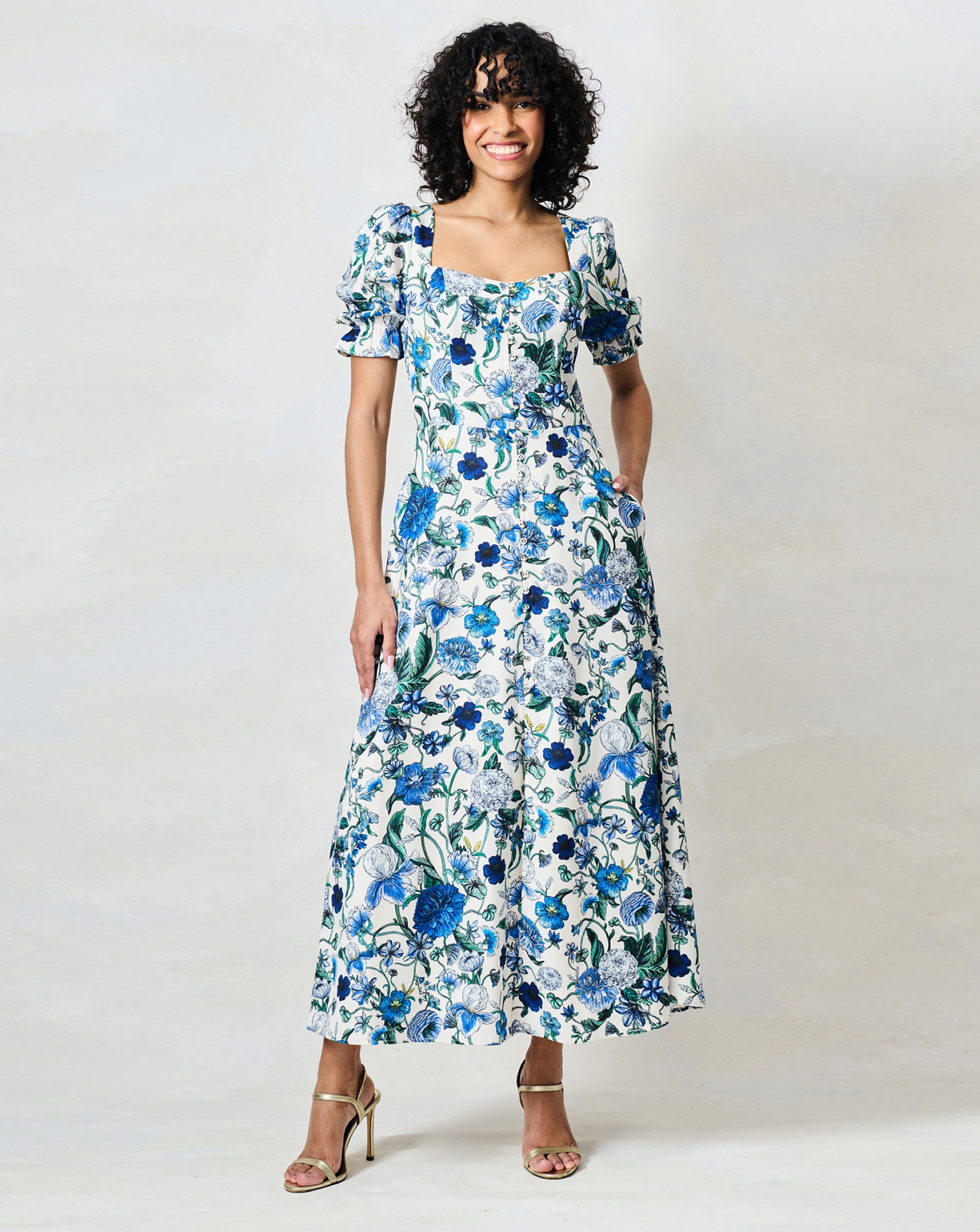 Person wearing a white Hope & Ivy midi dress with a blue floral print, and gold heeled sandals.