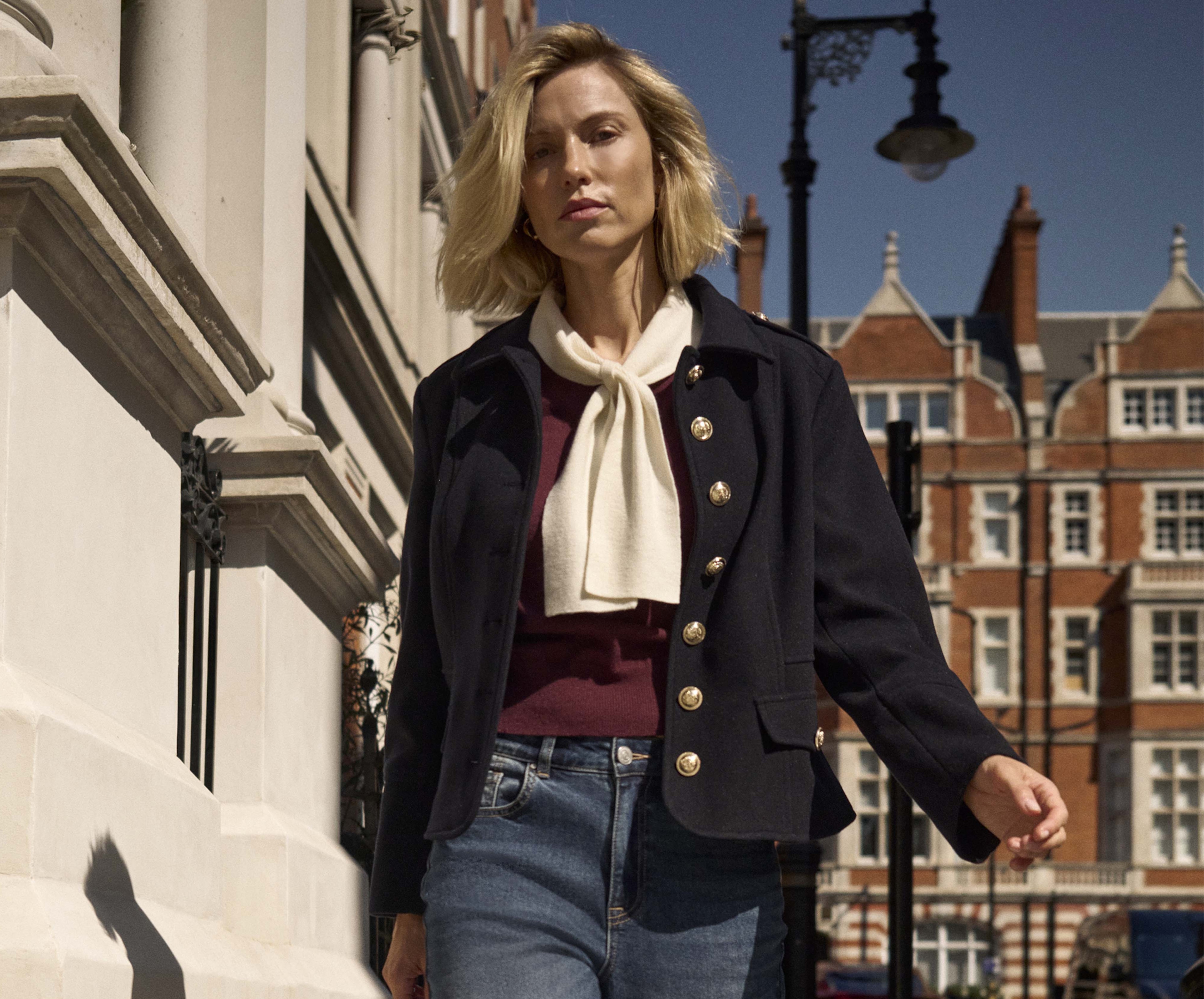 A woman walking on a street wearing a maroon jumper and blue jacket.