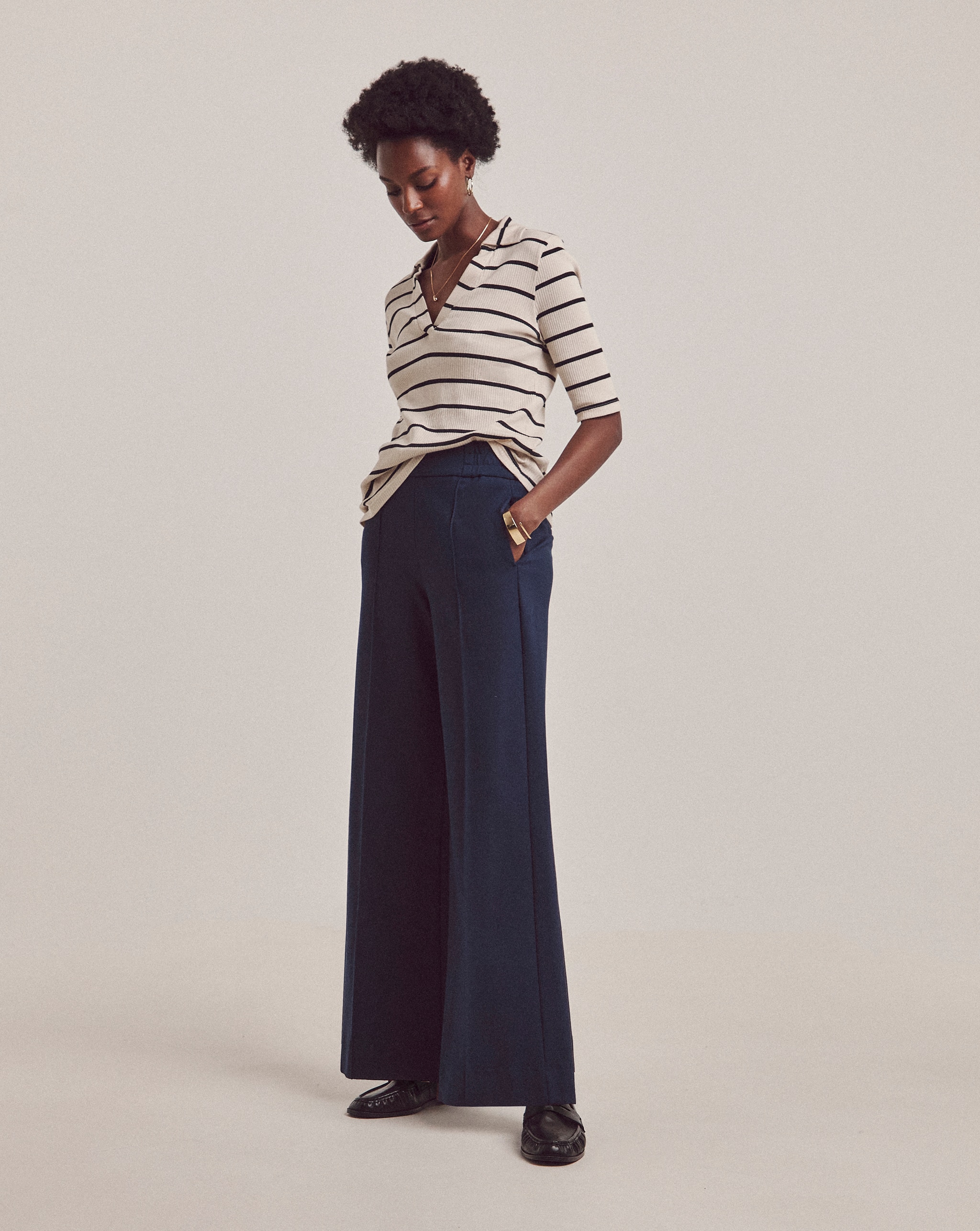 A woman wearing a striped v neck top with blue wide leg trousers.