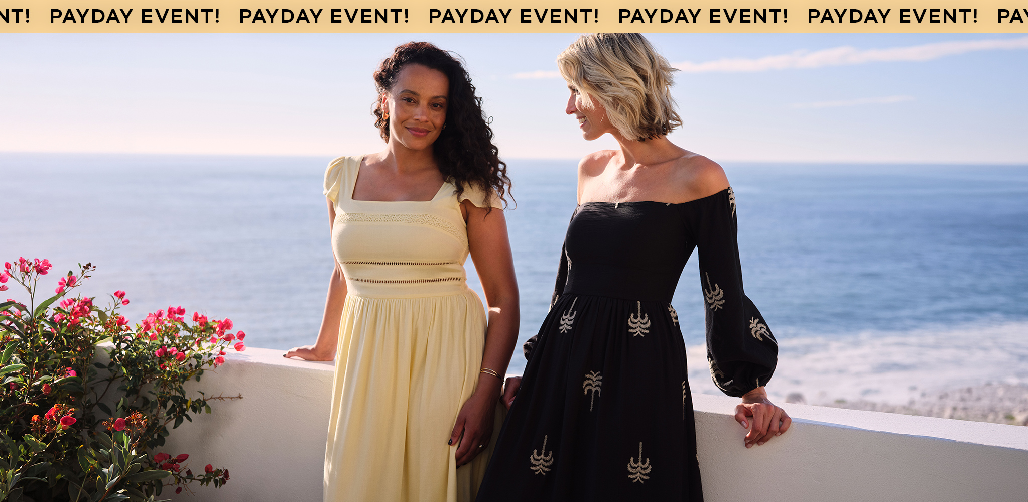 Two women wearing dresses perched on a balcony with the sea in the background.