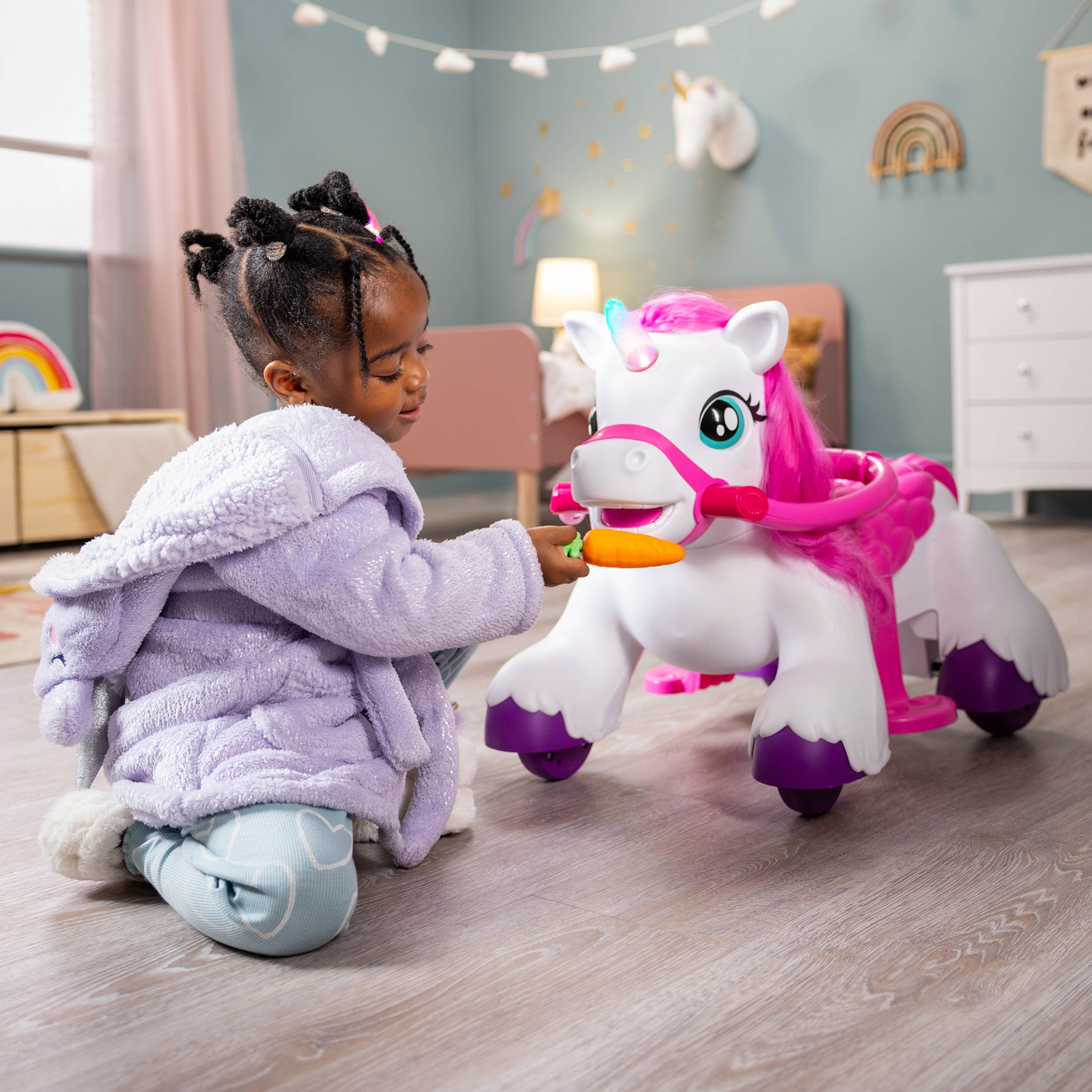 A little girl in a lilac dressing gown playing with a large toy horse with bright pink hair and accessories.