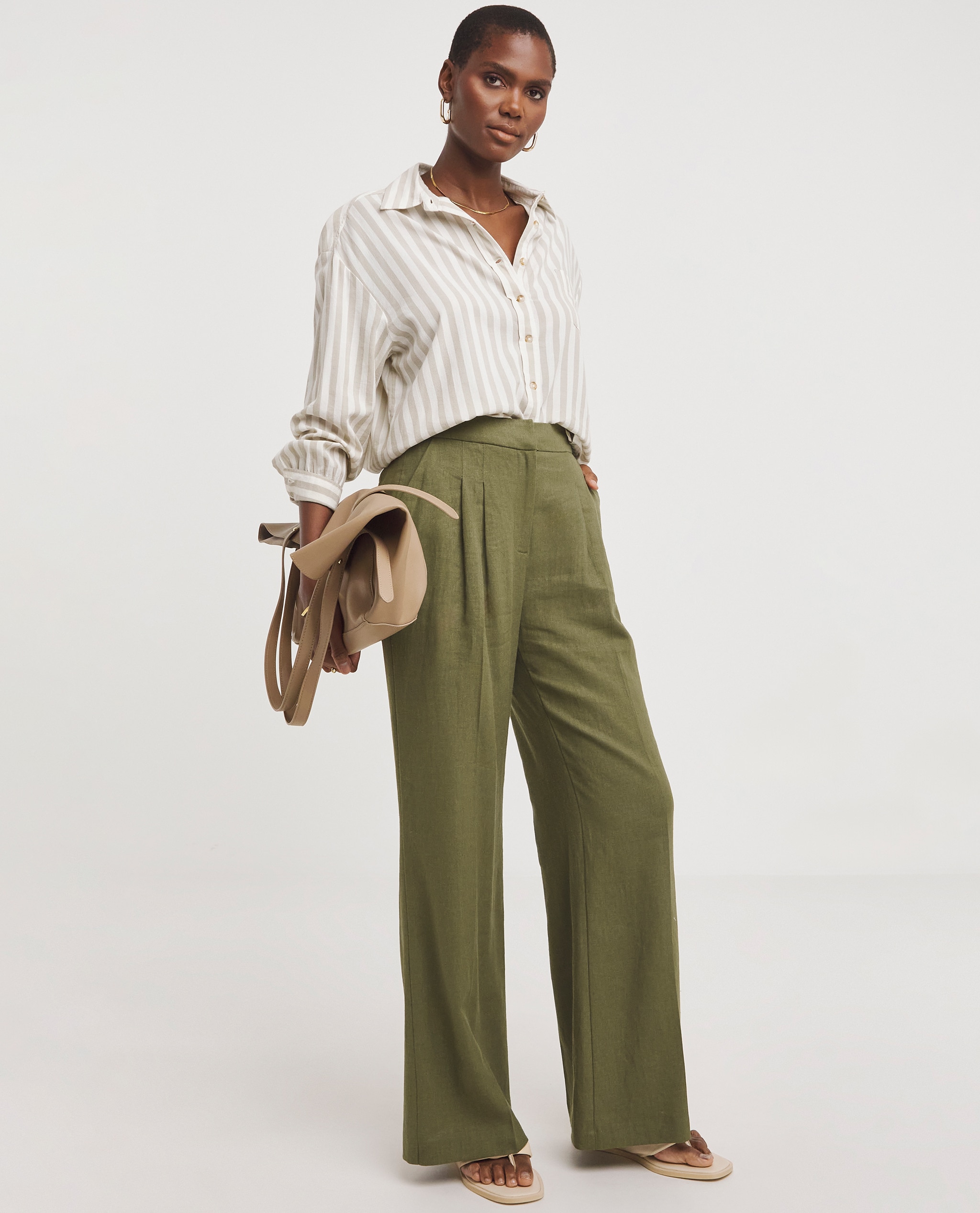 Model is wearing a stripe shirt with olive green linen pleated wide leg trousers.