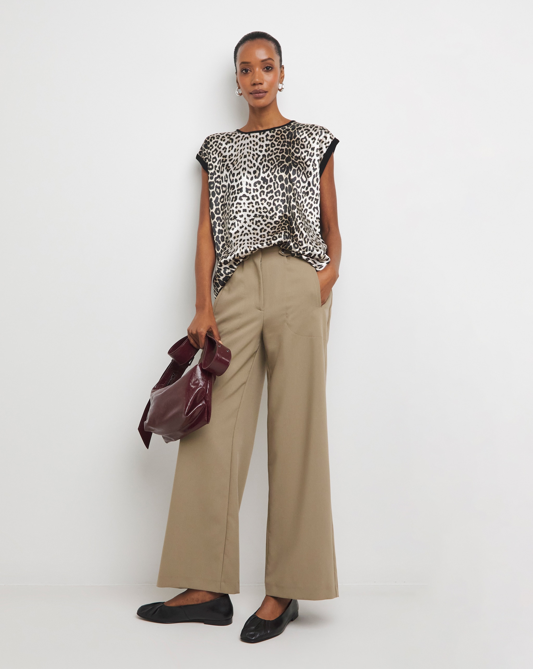 Person wearing a sheer leopard-print blouse over a black top with dark wide-leg jeans and cuffed hems.