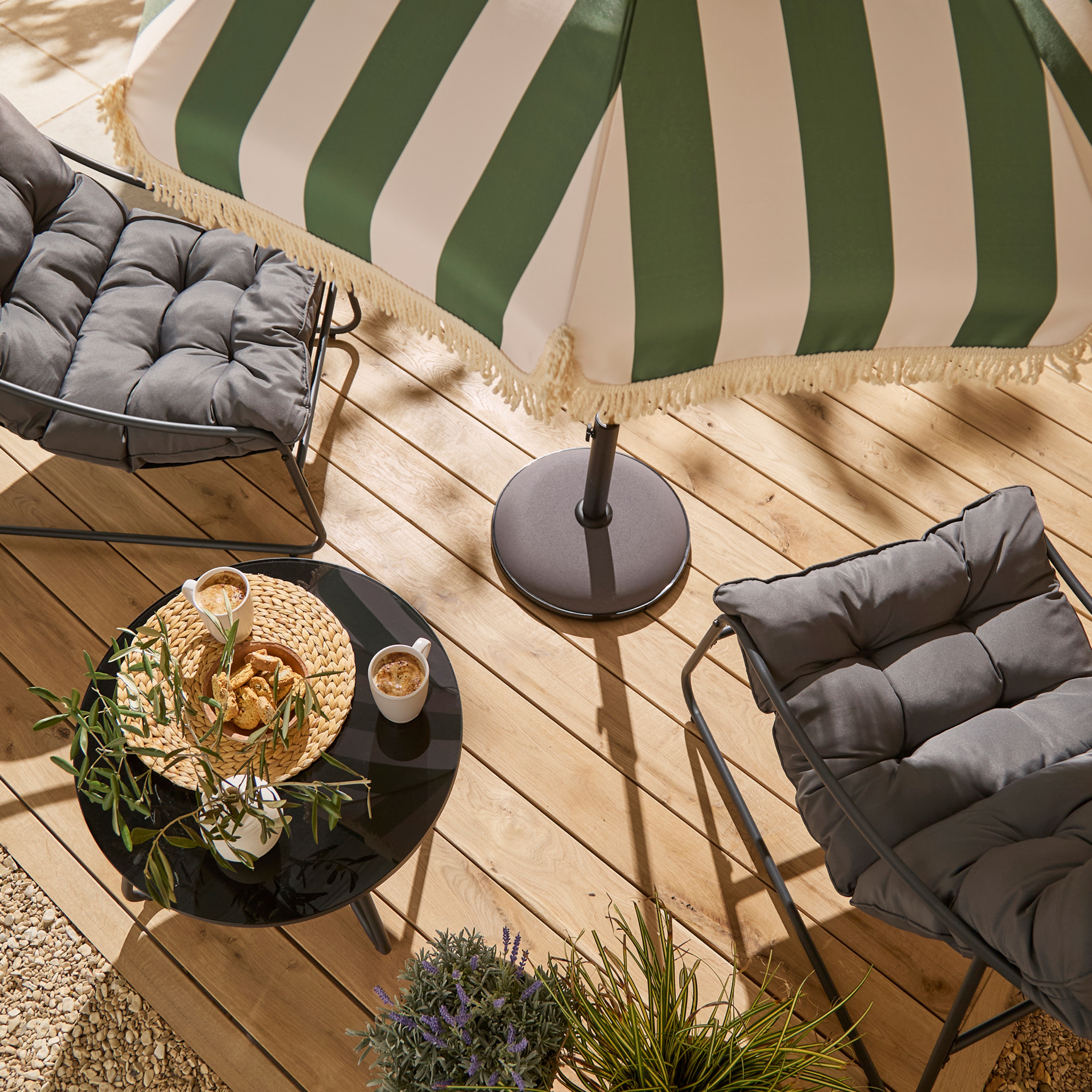 A garden scene with a green and beige striped parasol and two grey chairs