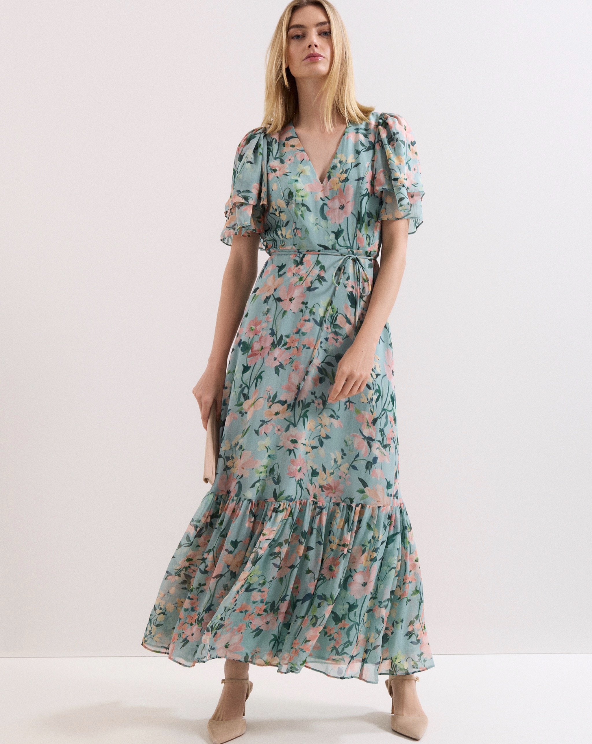 Person wearing a flowing blue-green floral maxi dress with puff sleeves, nude heels, and a clutch bag.
