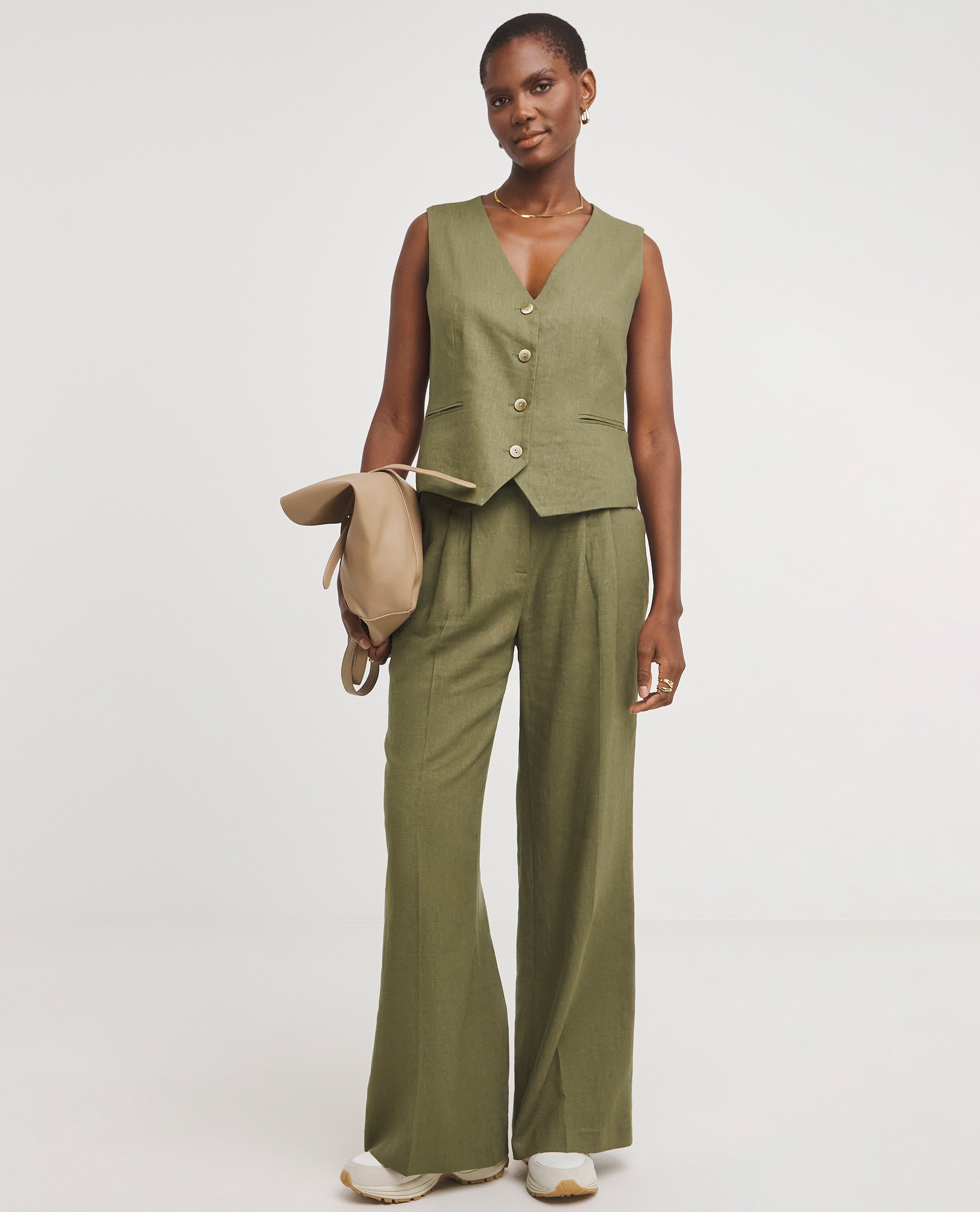 Model is wearing a olive green linen button front waistcoat with matching linen pleated wide leg trousers.