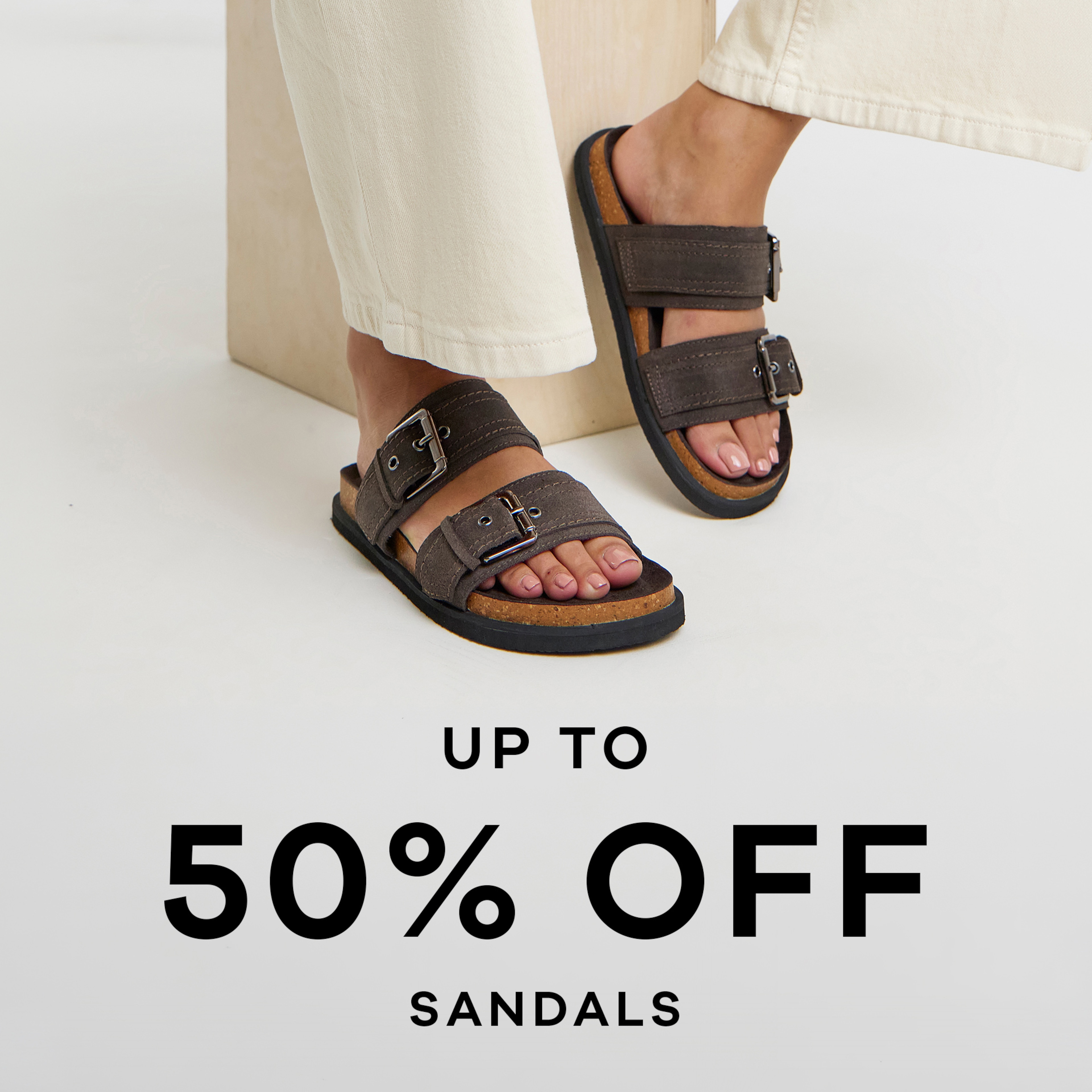 A person's feet wearing brown twin strap sandals. Up to 50% off sandals.