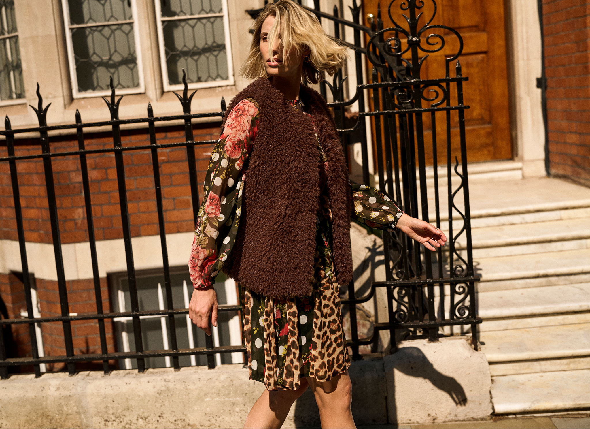 A woman walking on street looking behind her wearing a multi print and coloured georgette godet Dress
