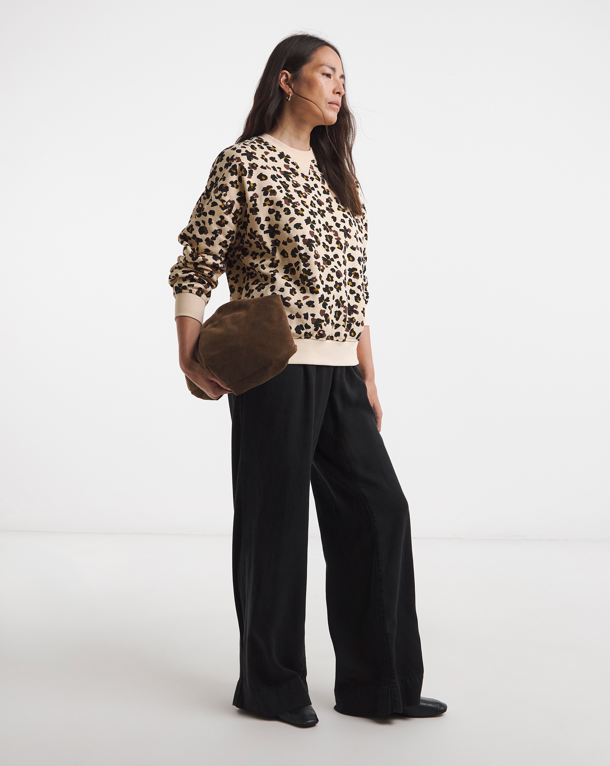 Person wearing a sleeveless leopard-print top with beige wide-leg trousers and black flats, holding a burgundy bag.