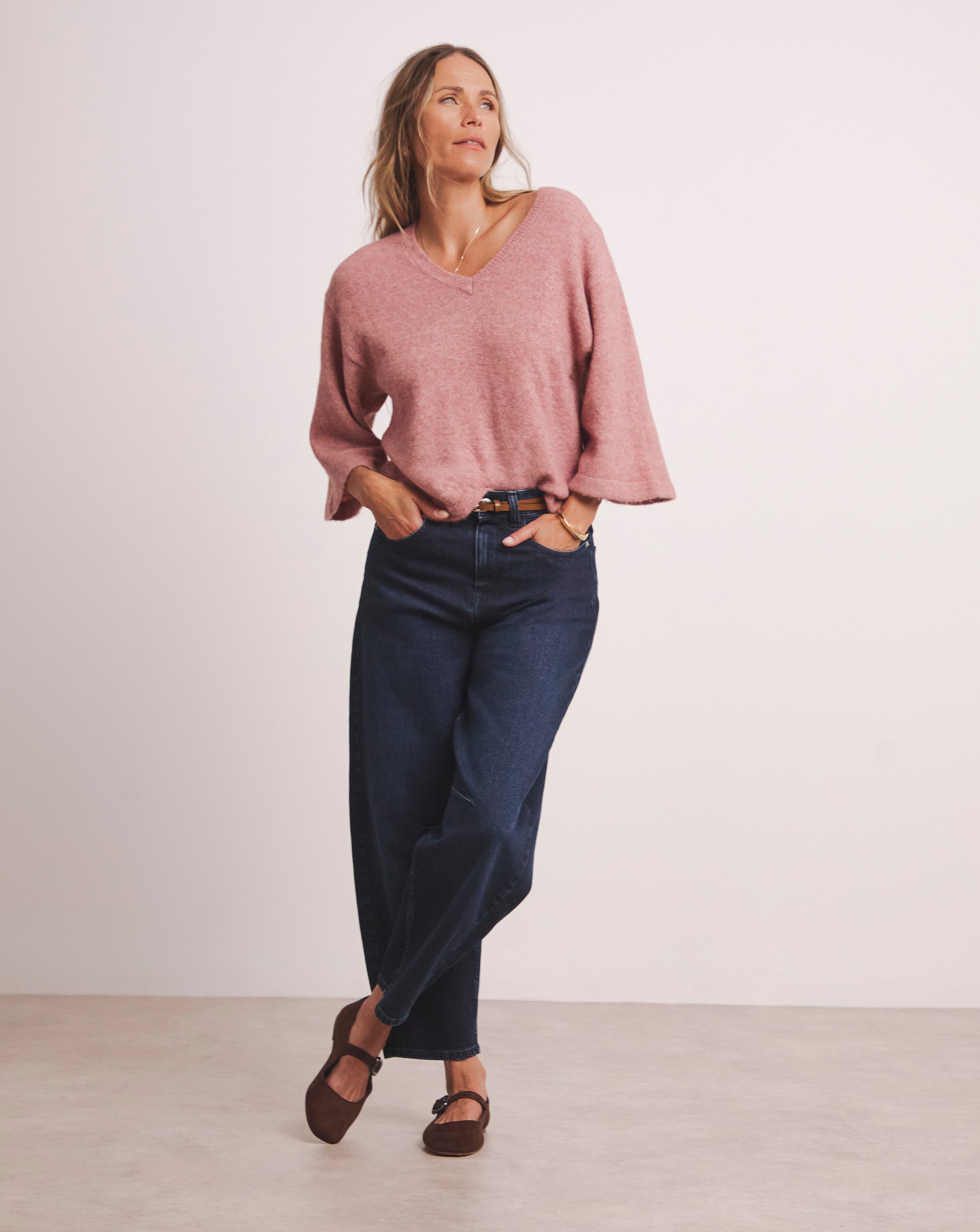 A woman wearing a pink v neck jumper with dark blue jeans.