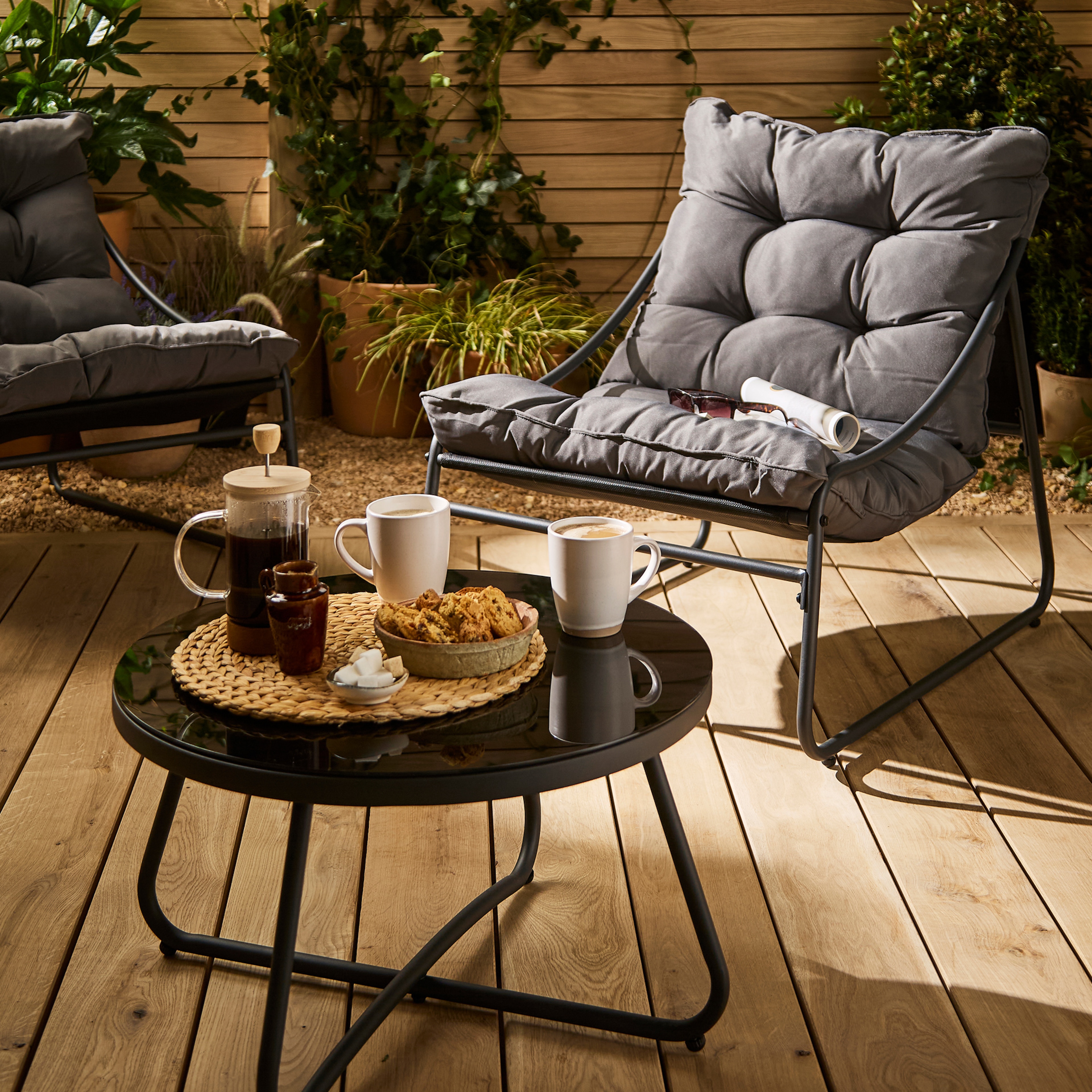 A garden with a grey chair and table with refreshments on it.