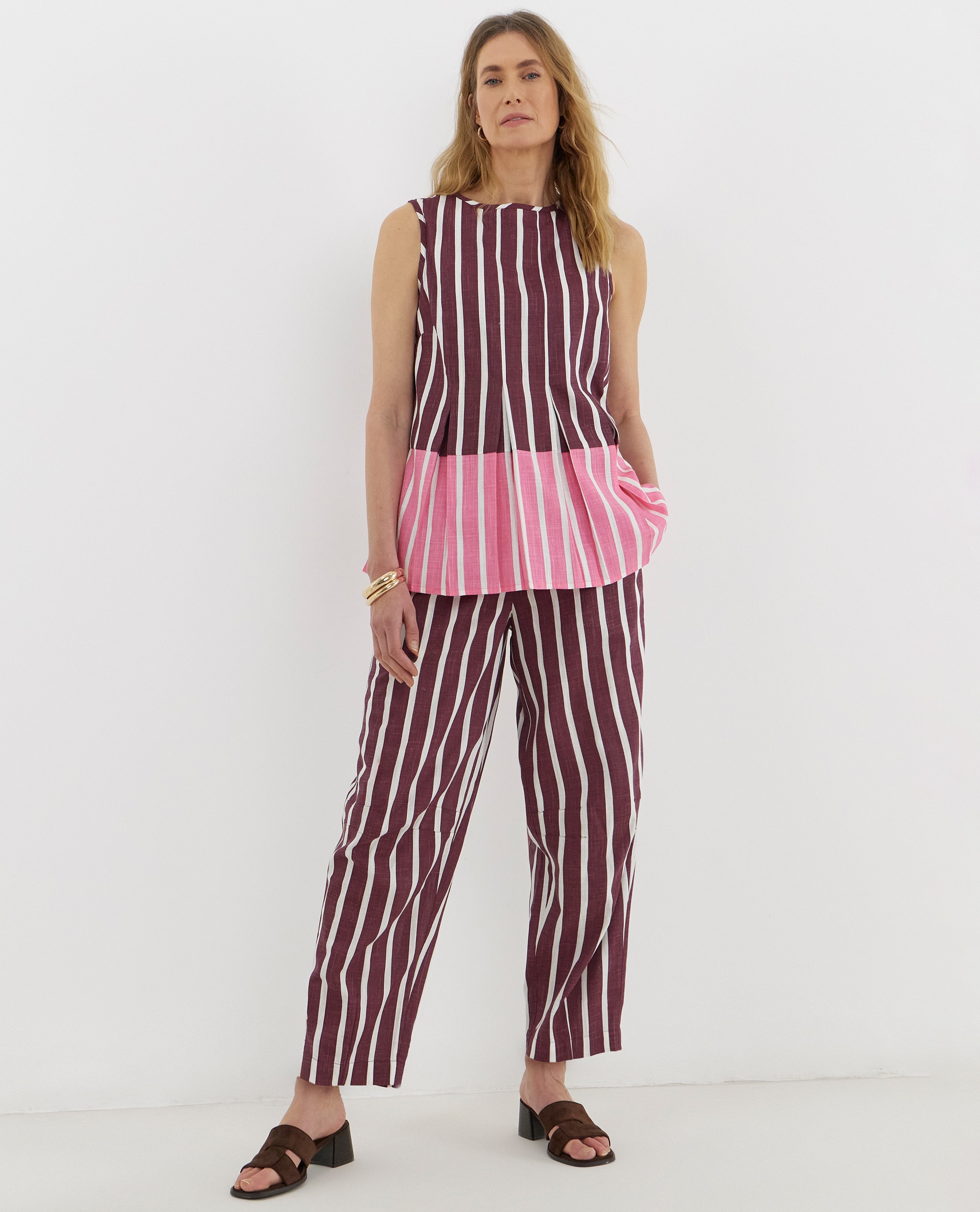 Model is wearing a linen mix pleated peplum shell top with a pair of plum stripe linen mix barrel leg trousers.