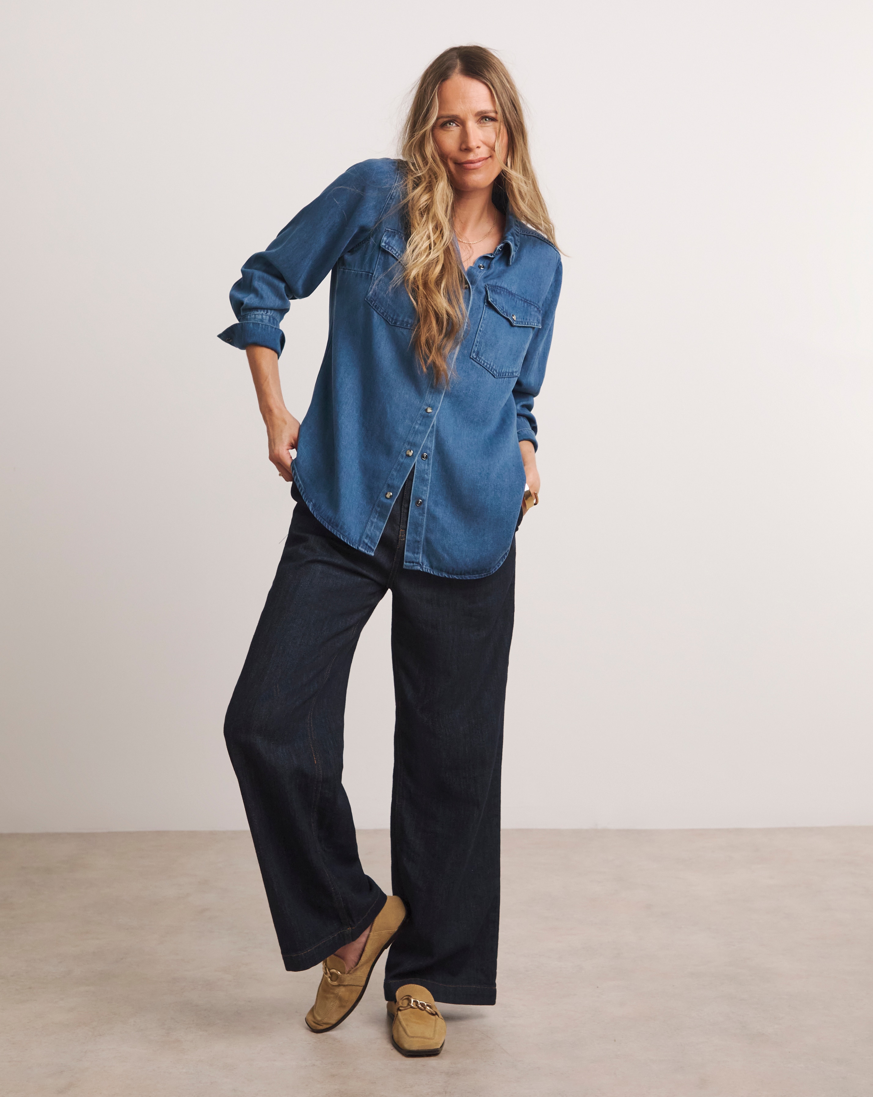 A woman wearing a long sleeved denim shirt with blue trousers.