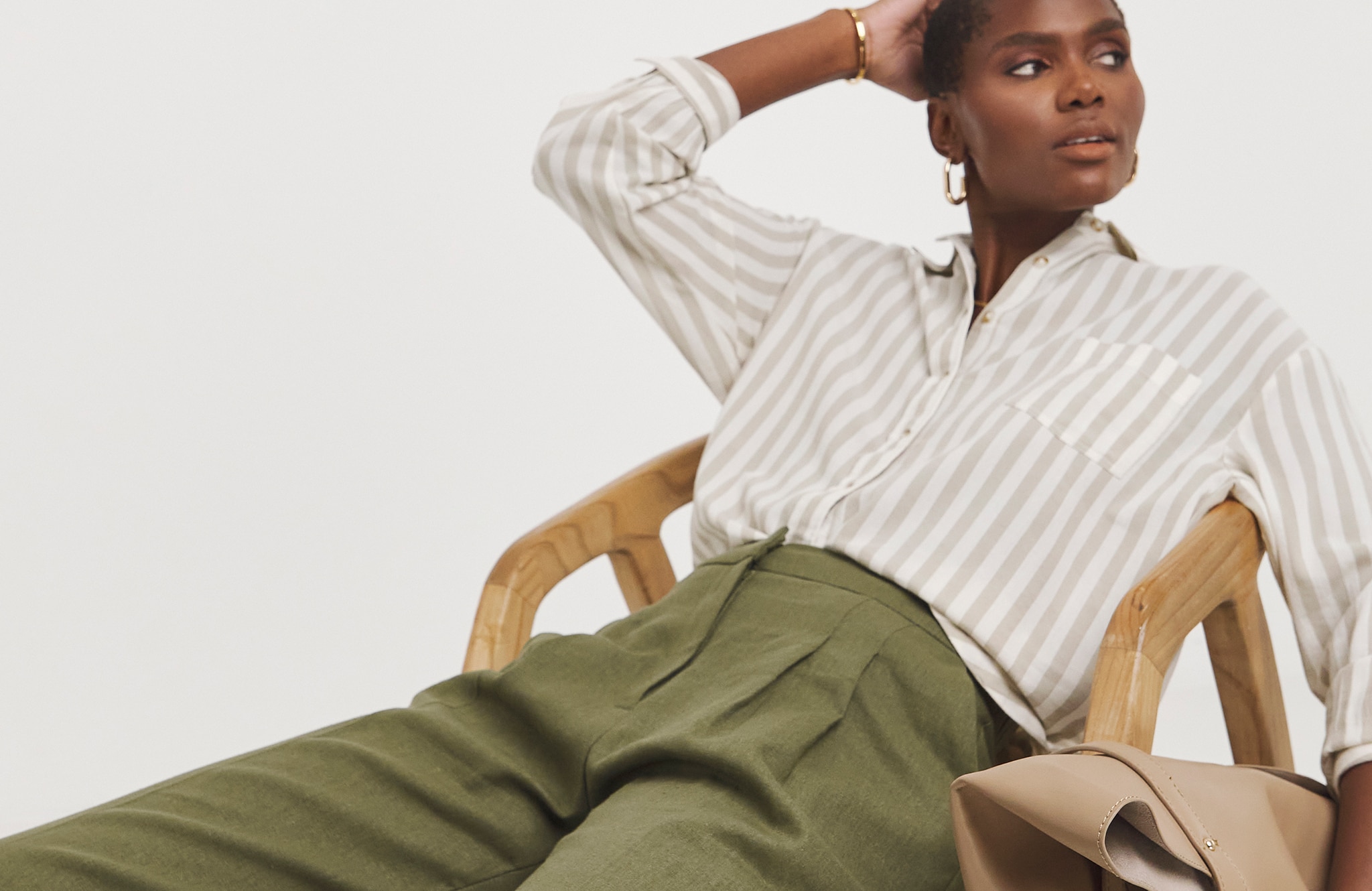Model is wearing a stripe shirt with olive green linen pleated wide leg trousers.