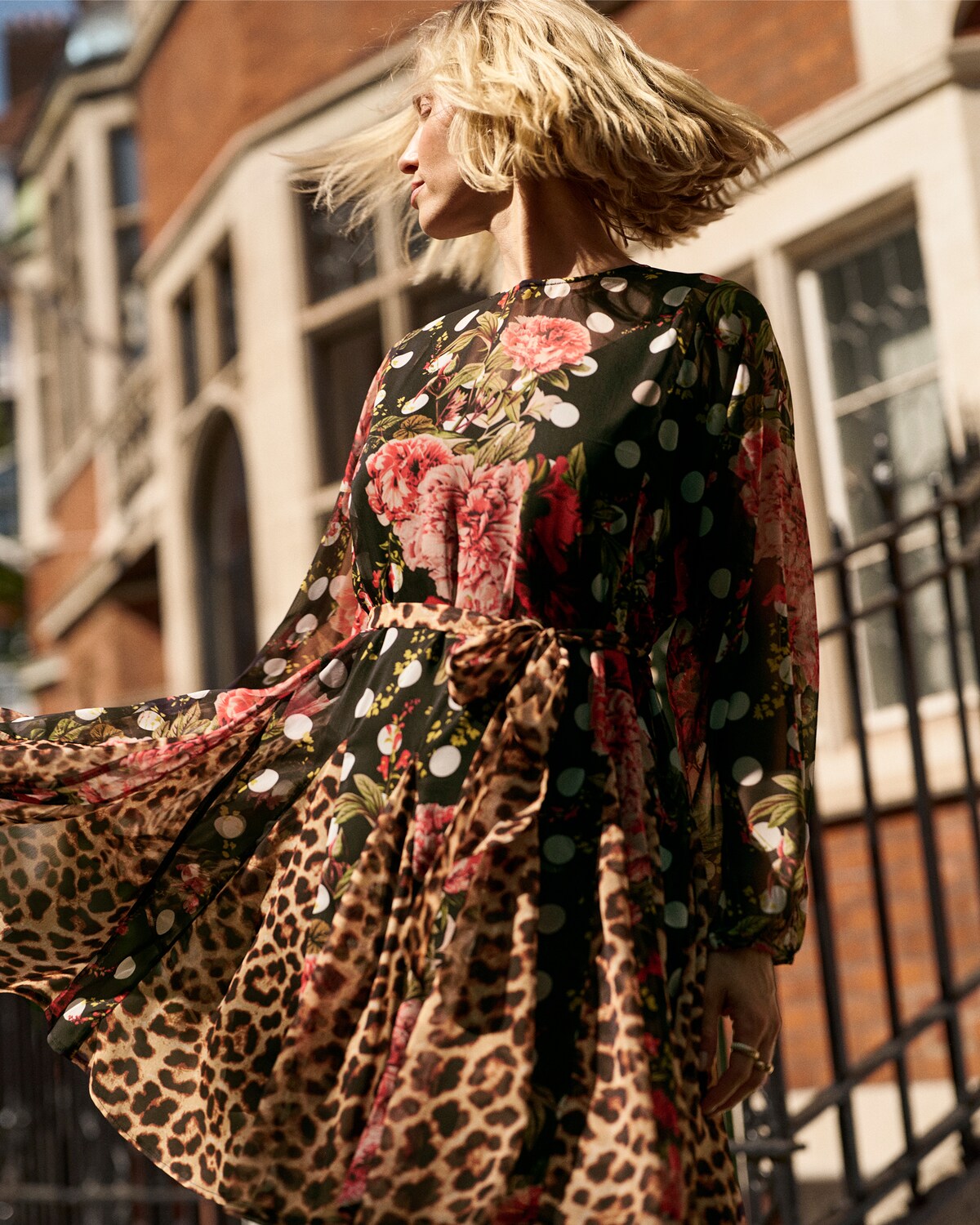 A woman swishing the hem of her colourful print dress around on a street.
