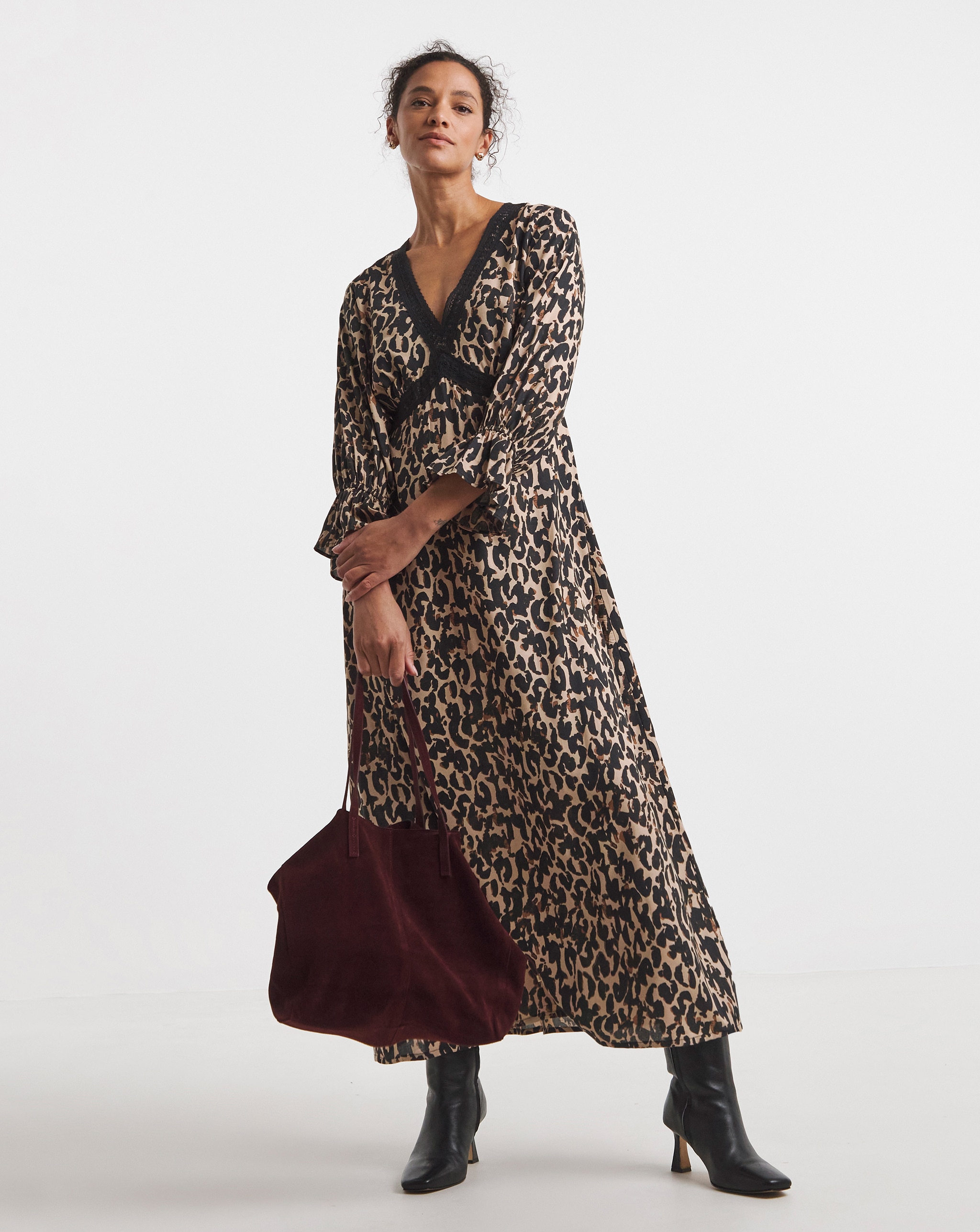 Person wearing a long leopard-print wrap-style dress with black ankle boots, carrying a burgundy tote bag.
