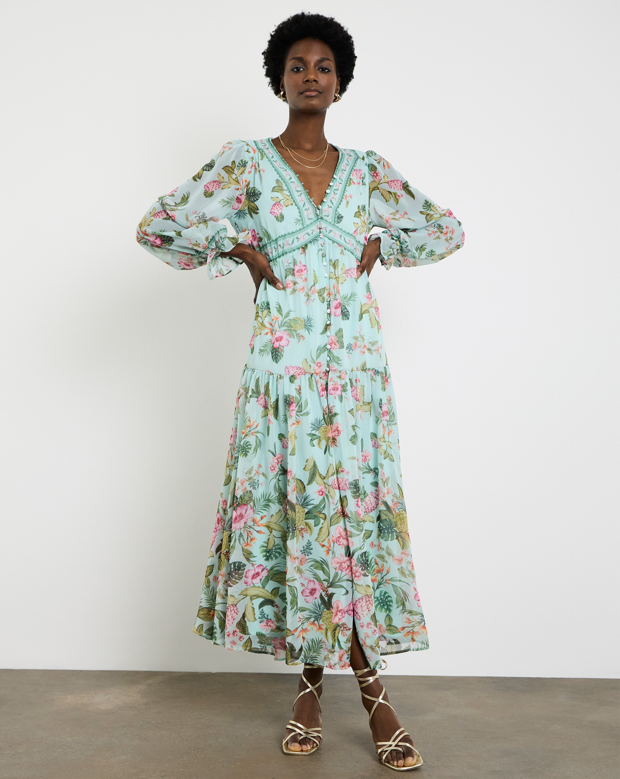 Person wearing a mint-green Joanna Hope floral maxi dress with long sleeves and gold strappy sandals.