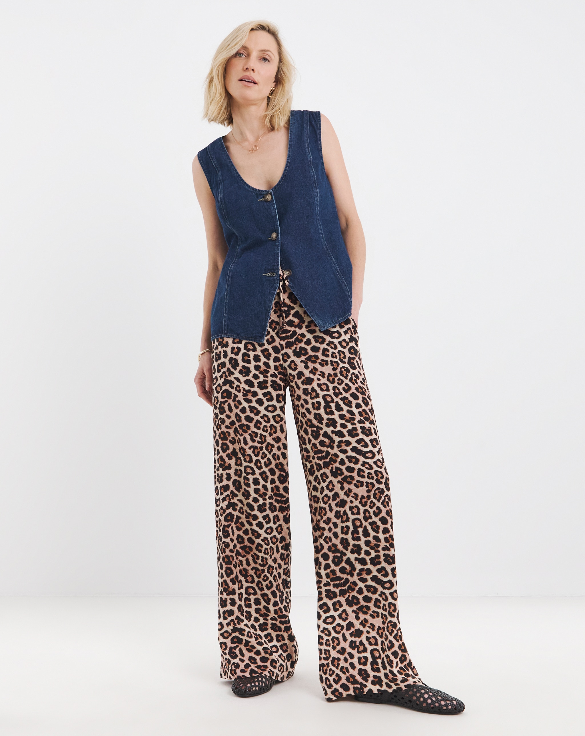 Person wearing a sleeveless denim waistcoat with leopard-print wide-leg trousers and flat black shoes.