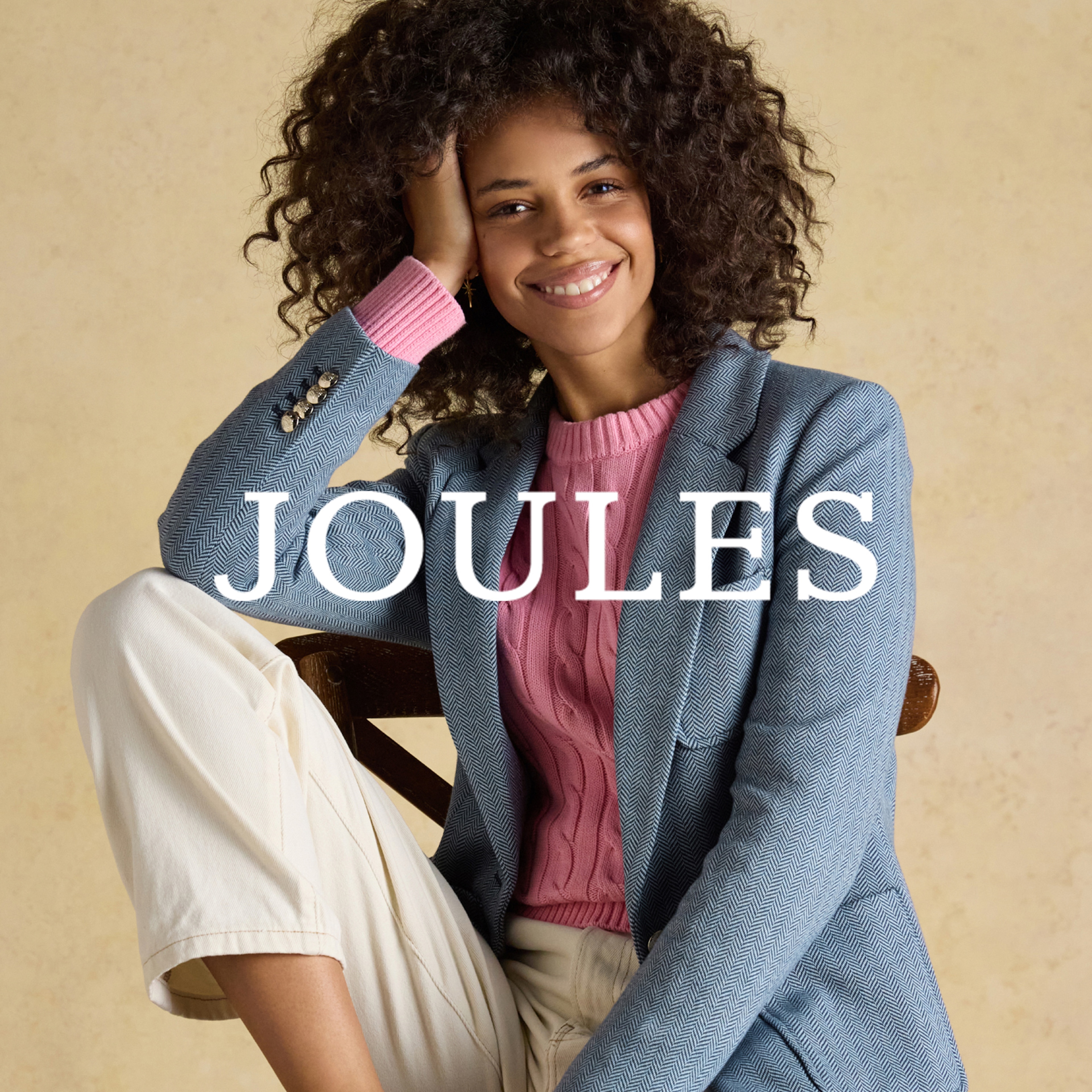 A lady sat wearing a blue blazer with a pink cable knit jumper underneath