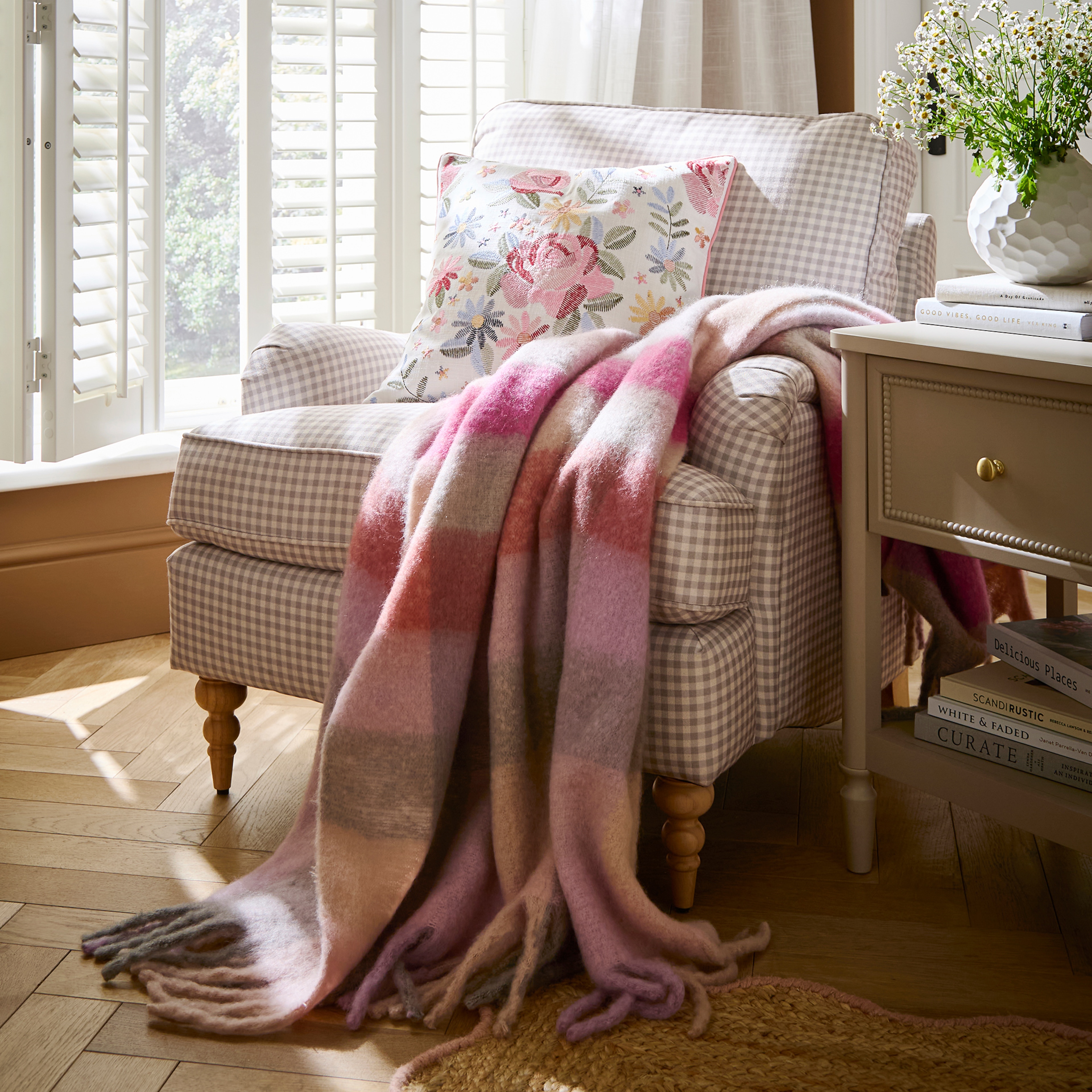 A gingham armchair in a room by a window with a pink check blanket thrown over it.