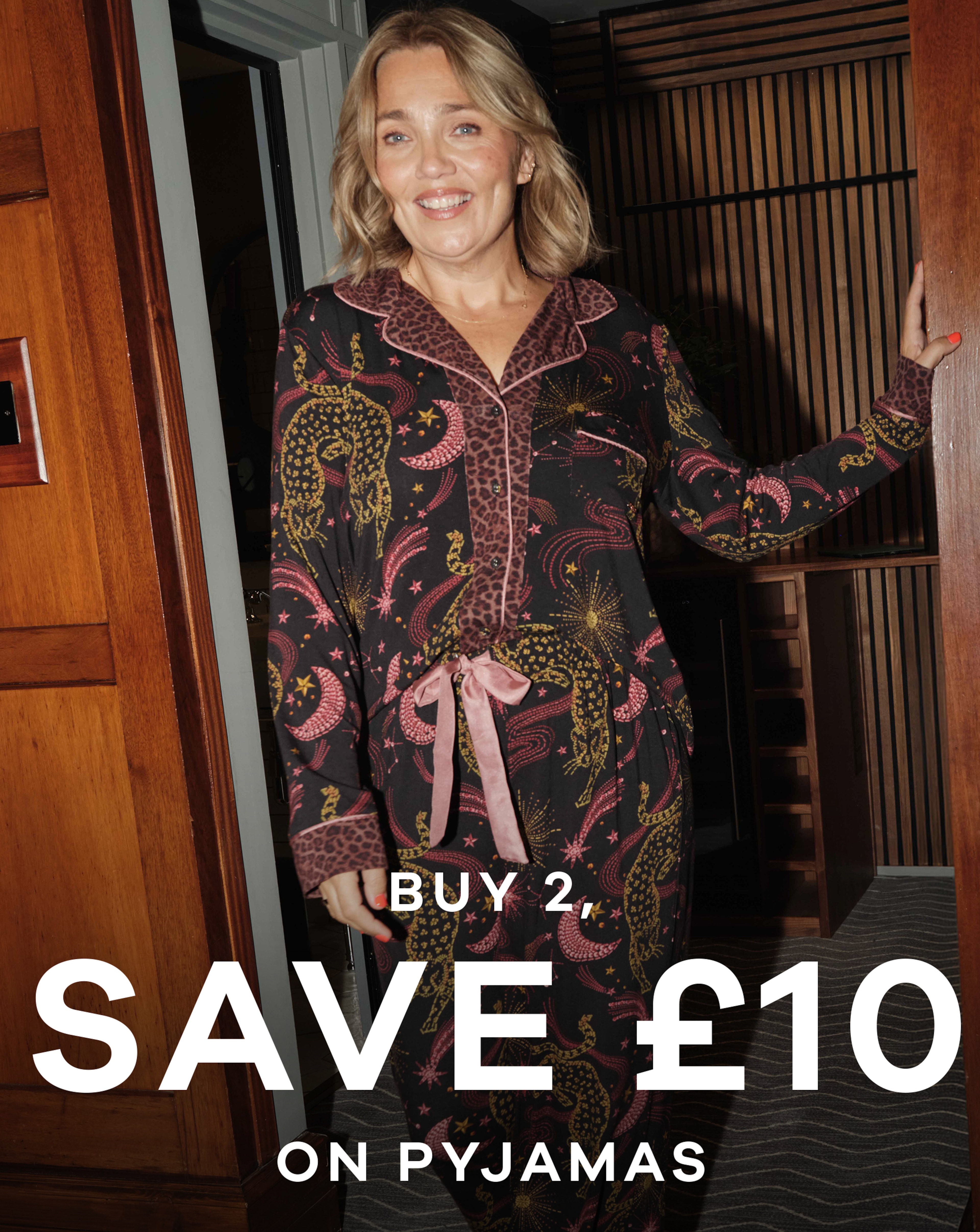 A woman stood in a doorway wearing black, pink and gold pyjama's.