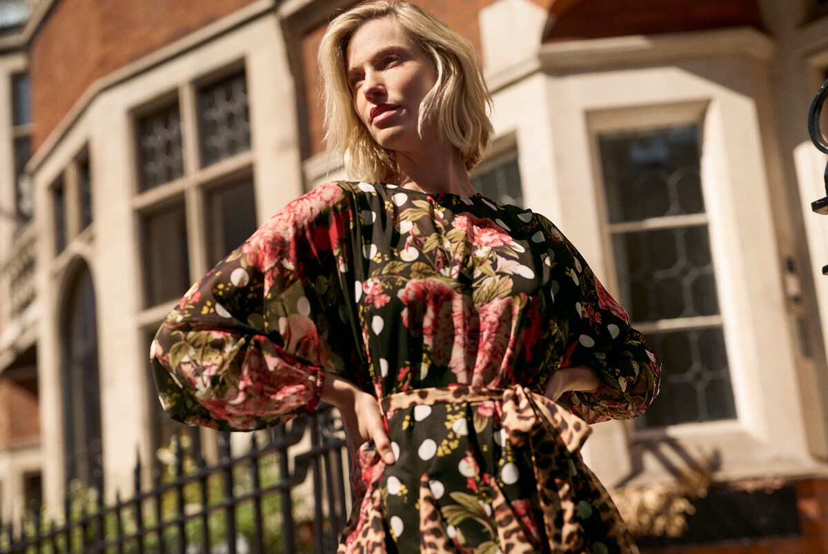 Person wearing a floral and polka-dot midi dress with sheer balloon sleeves and a leopard-print waist tie, photographed outdoors.