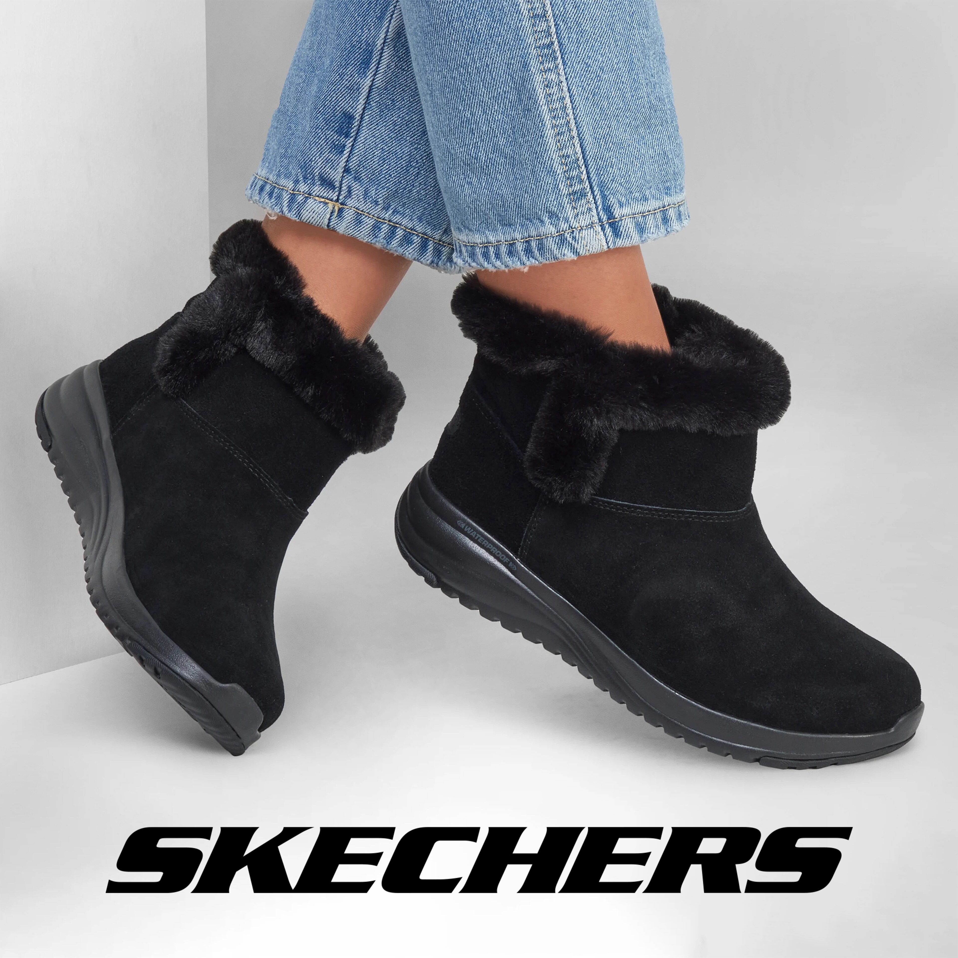 A pair of legs from the shin below in pale blue jeans and wearing black Skechers ankle boots.