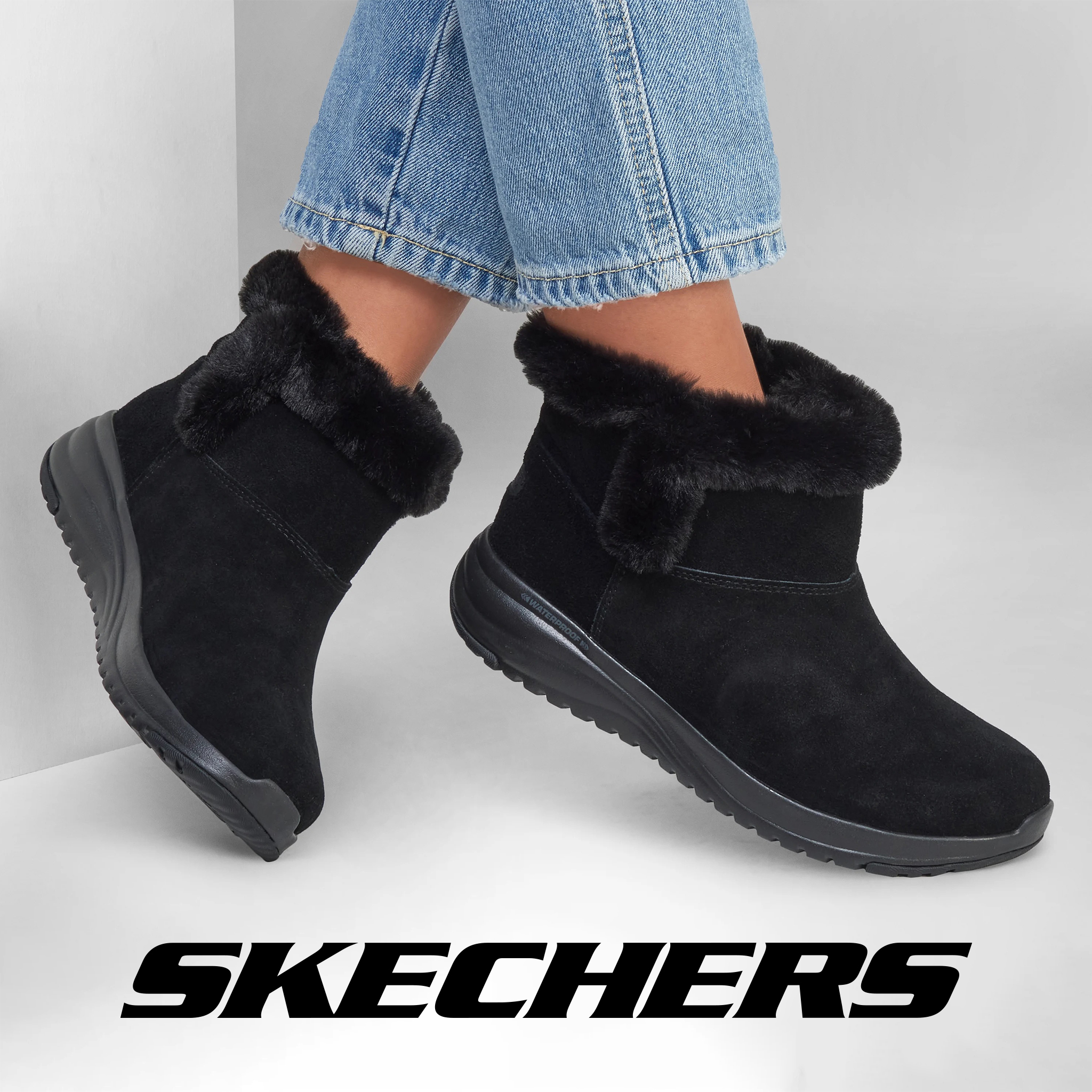 A pair of legs from the shin below in pale blue jeans and wearing black Skechers ankle boots.