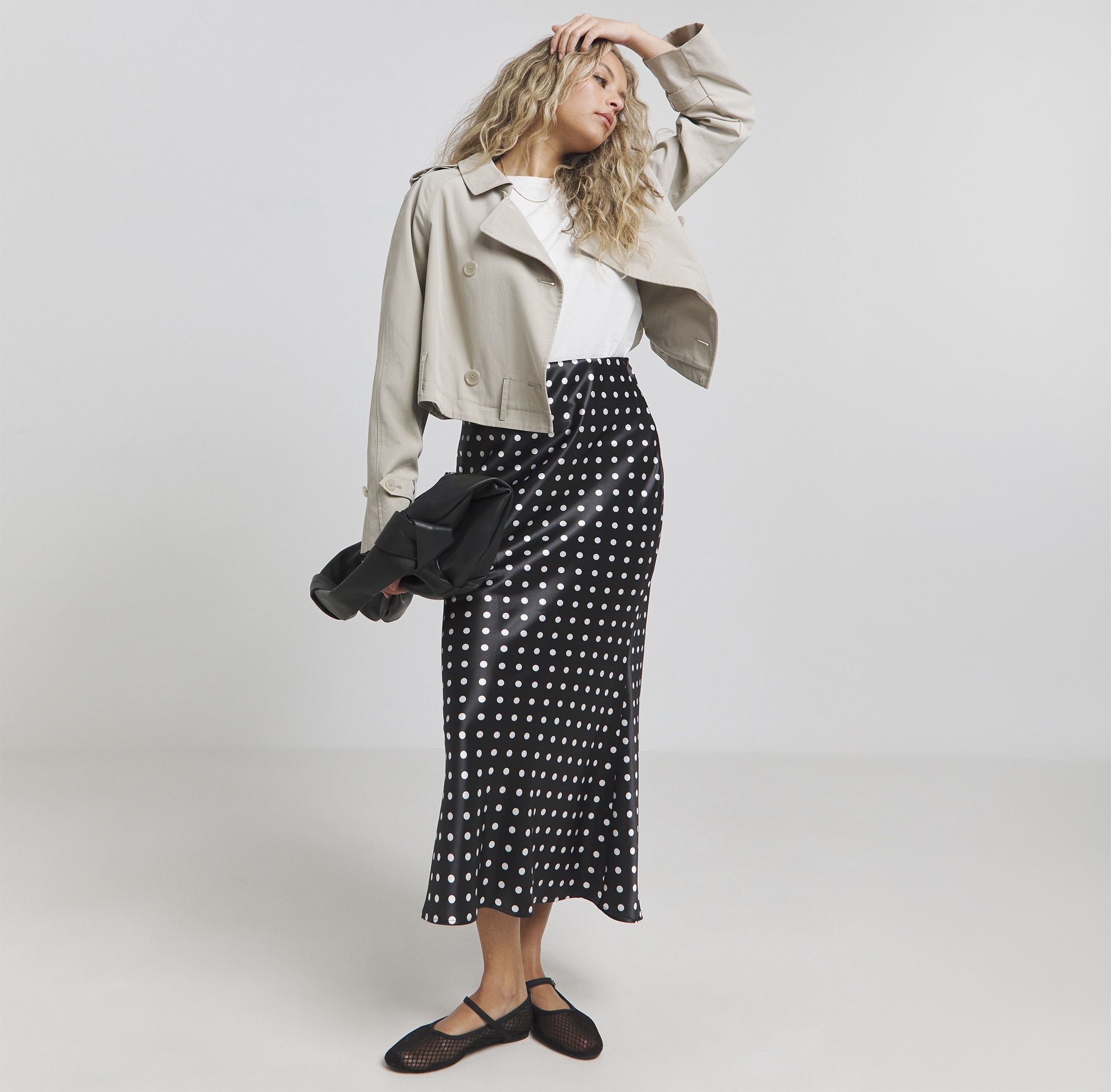 A lady wearing a satin maxi dress with a white t-shirt and stone coloured jacket.