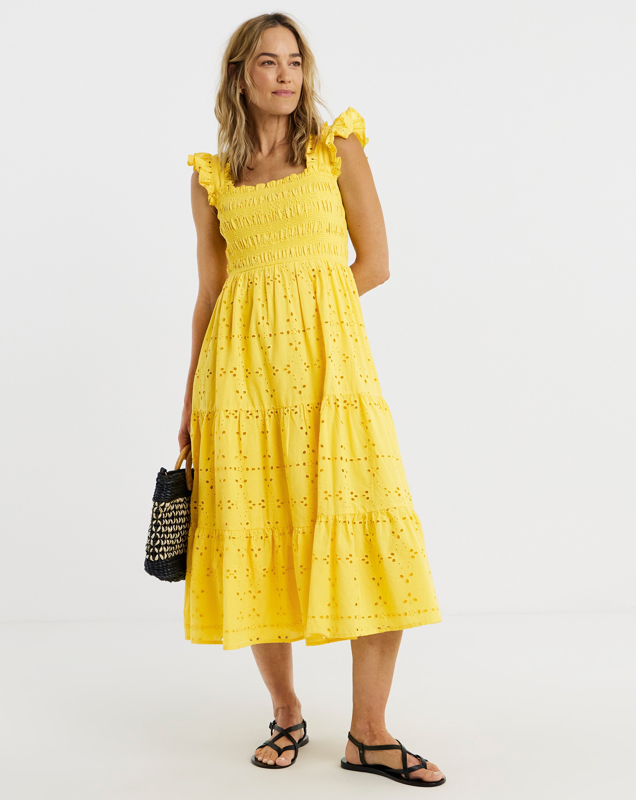 Person wearing a bright yellow tiered broderie anglaise midi dress with black sandals, carrying a woven tote bag.