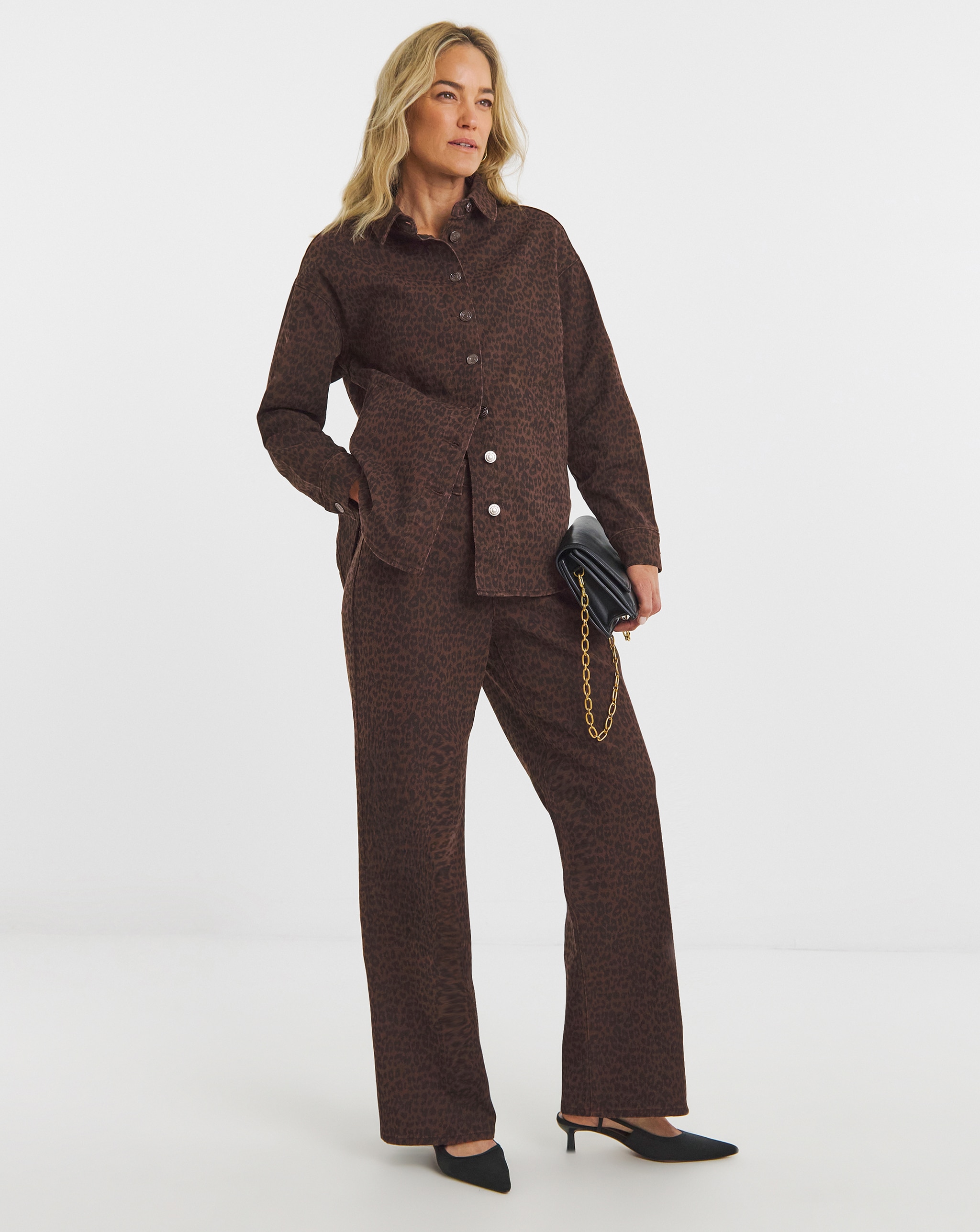 Person wearing a brown leopard-print shirt and matching trousers, holding a black clutch bag with gold chain detail.