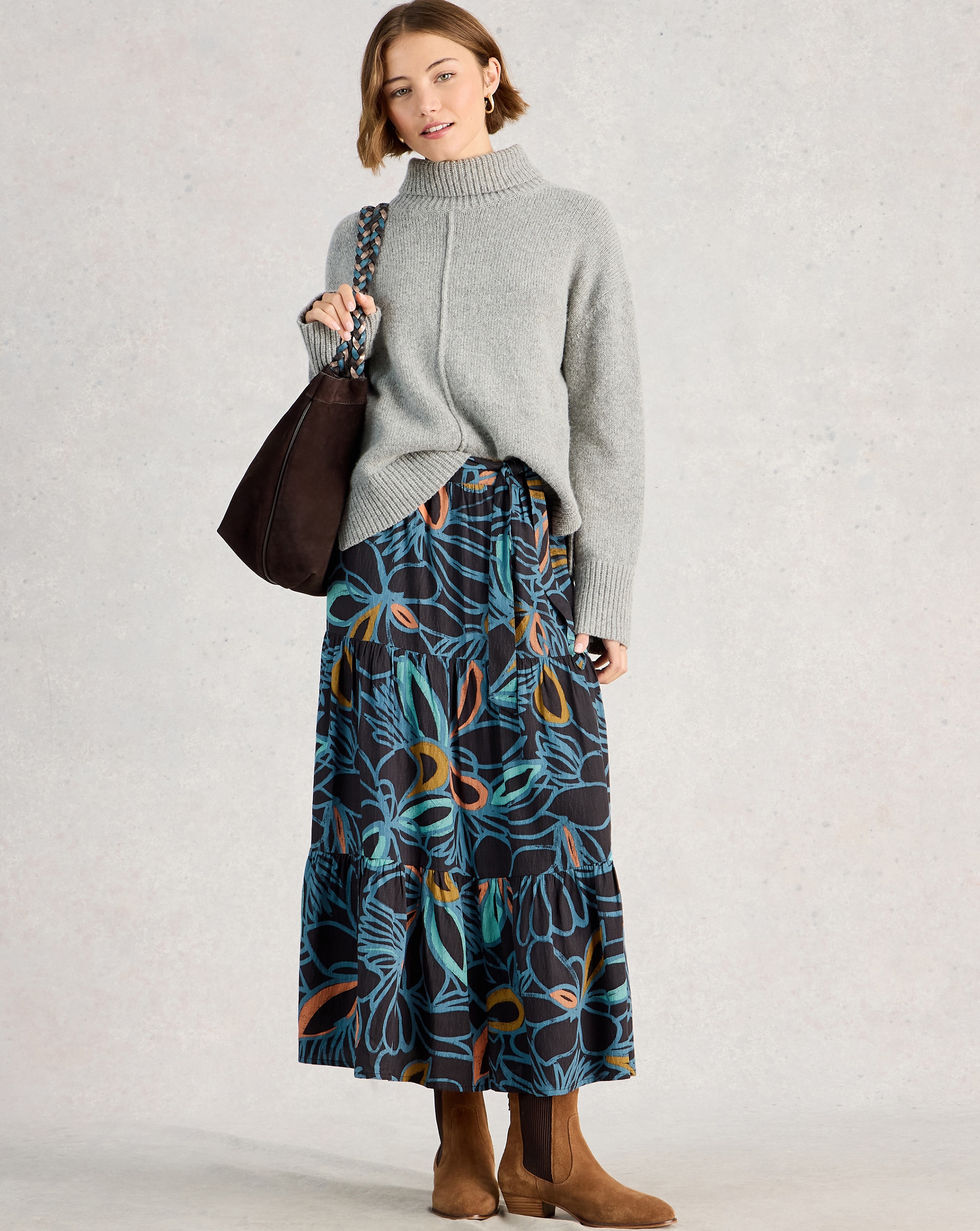 A lady wearing a grey roll neck jumper with a blue and and black flowery print maxi skirt