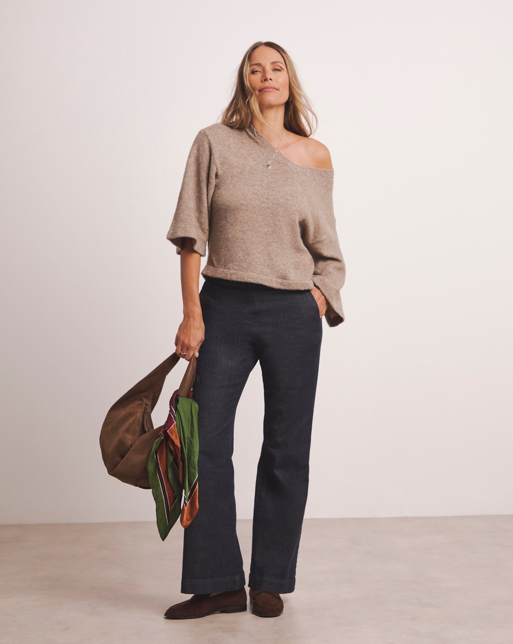 A woman wearing a light brown drop shoulder jumper with blue trousers.