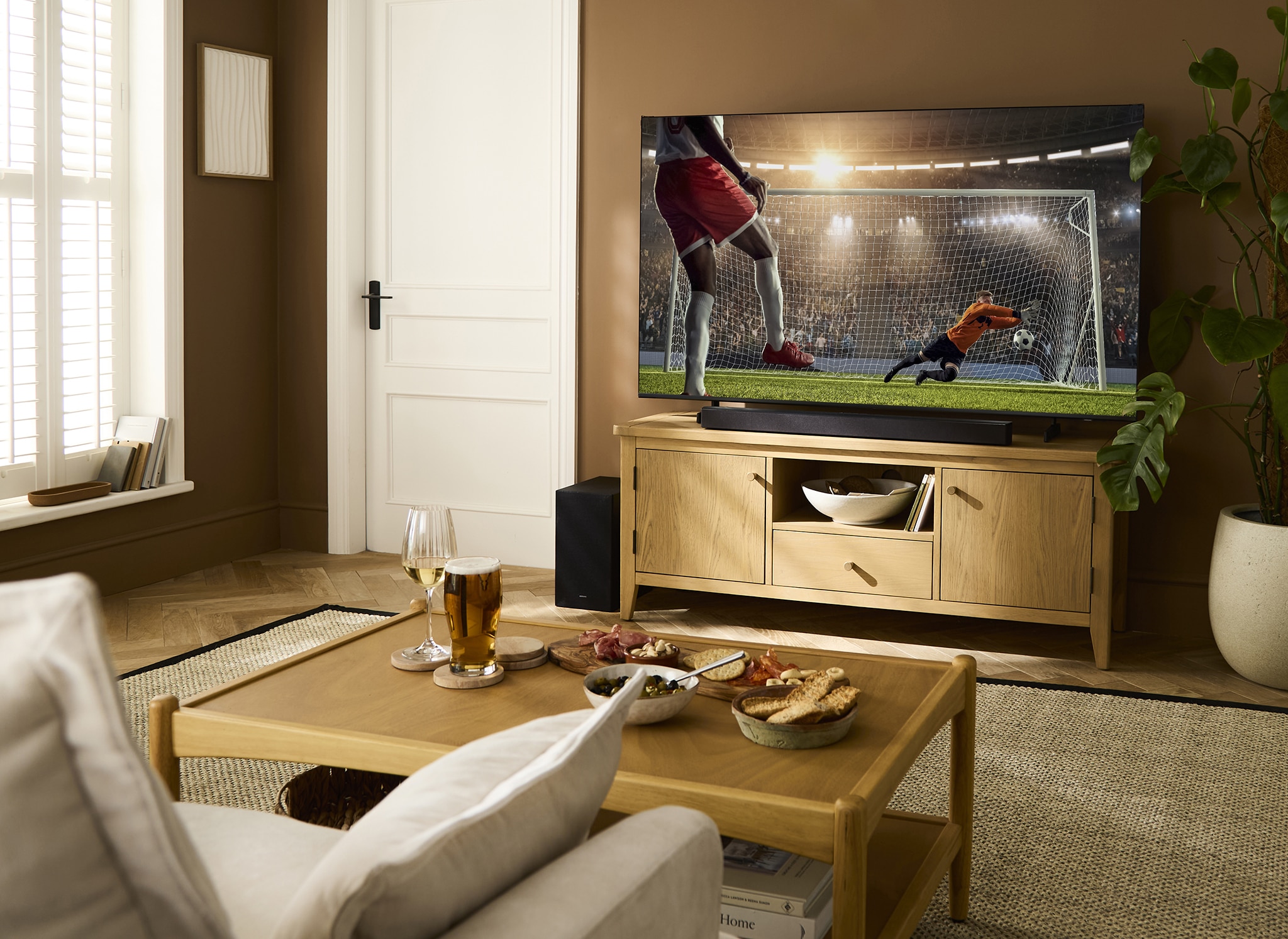 A living room with a TV on a unit displaying a football match in process.