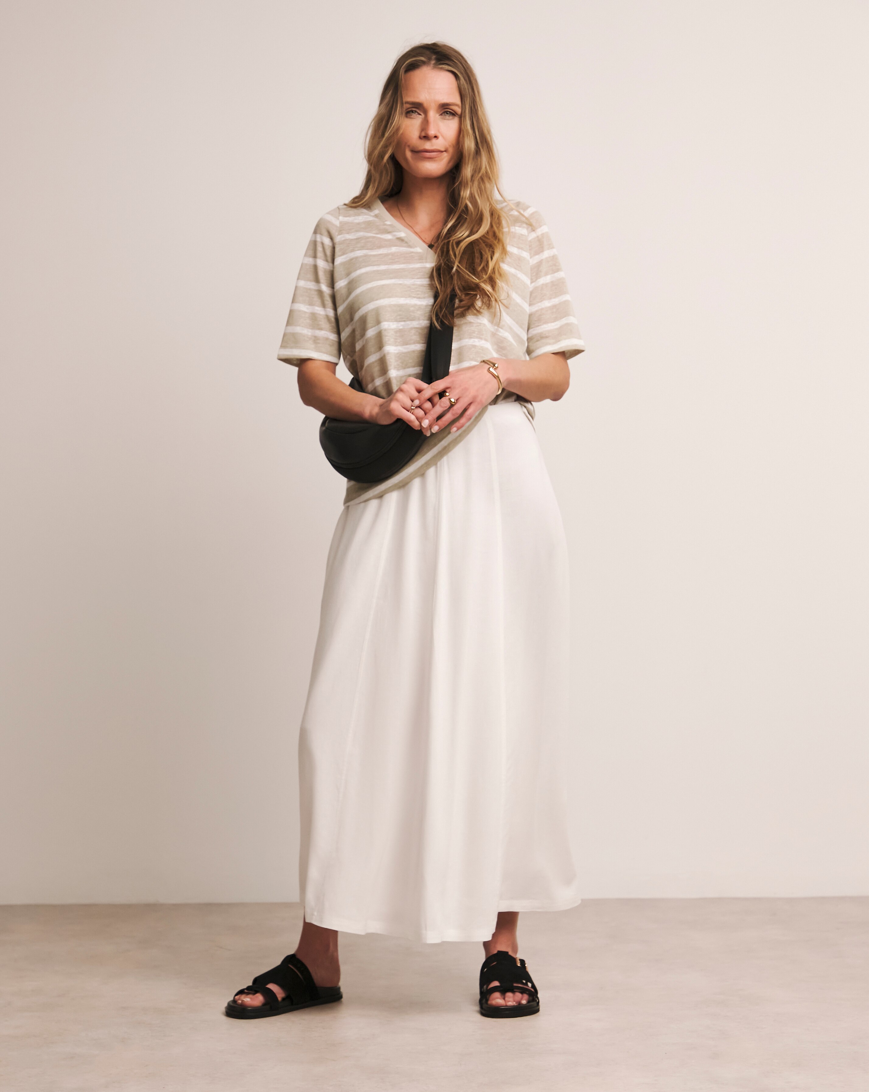 A woman wearing a stone and white coloured v neck top with a white skirt.
