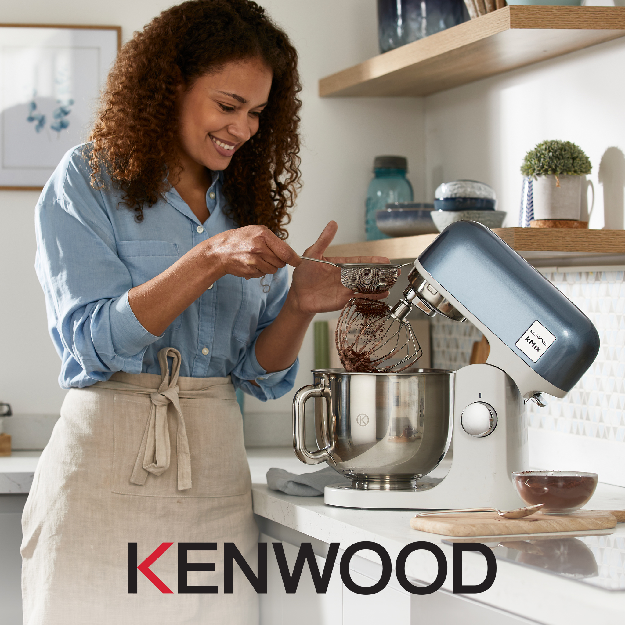 A womany using a Kenwood food mixing appliance in a kitchen.