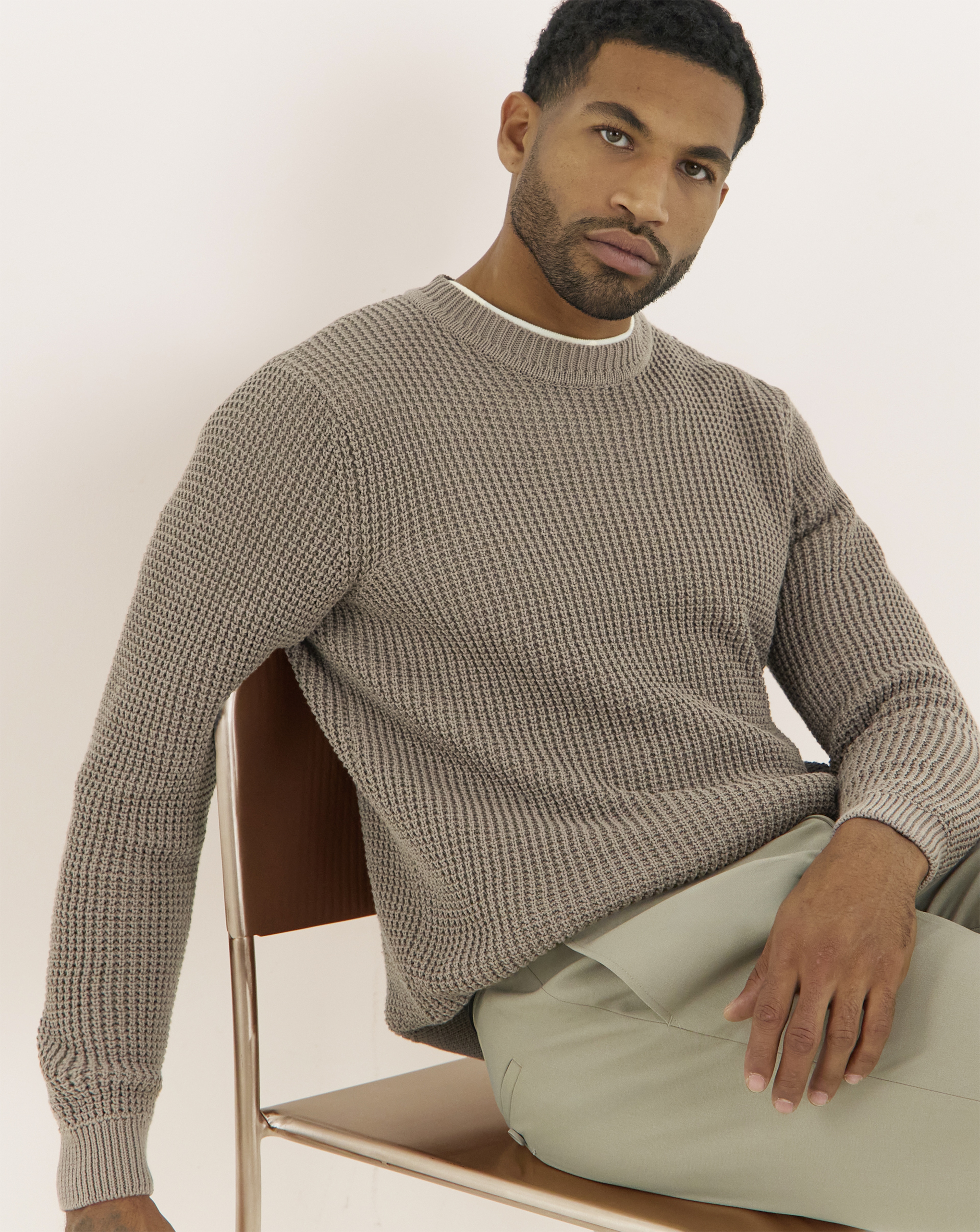A man sat in a chair wearing a brown textured crew neck jumper