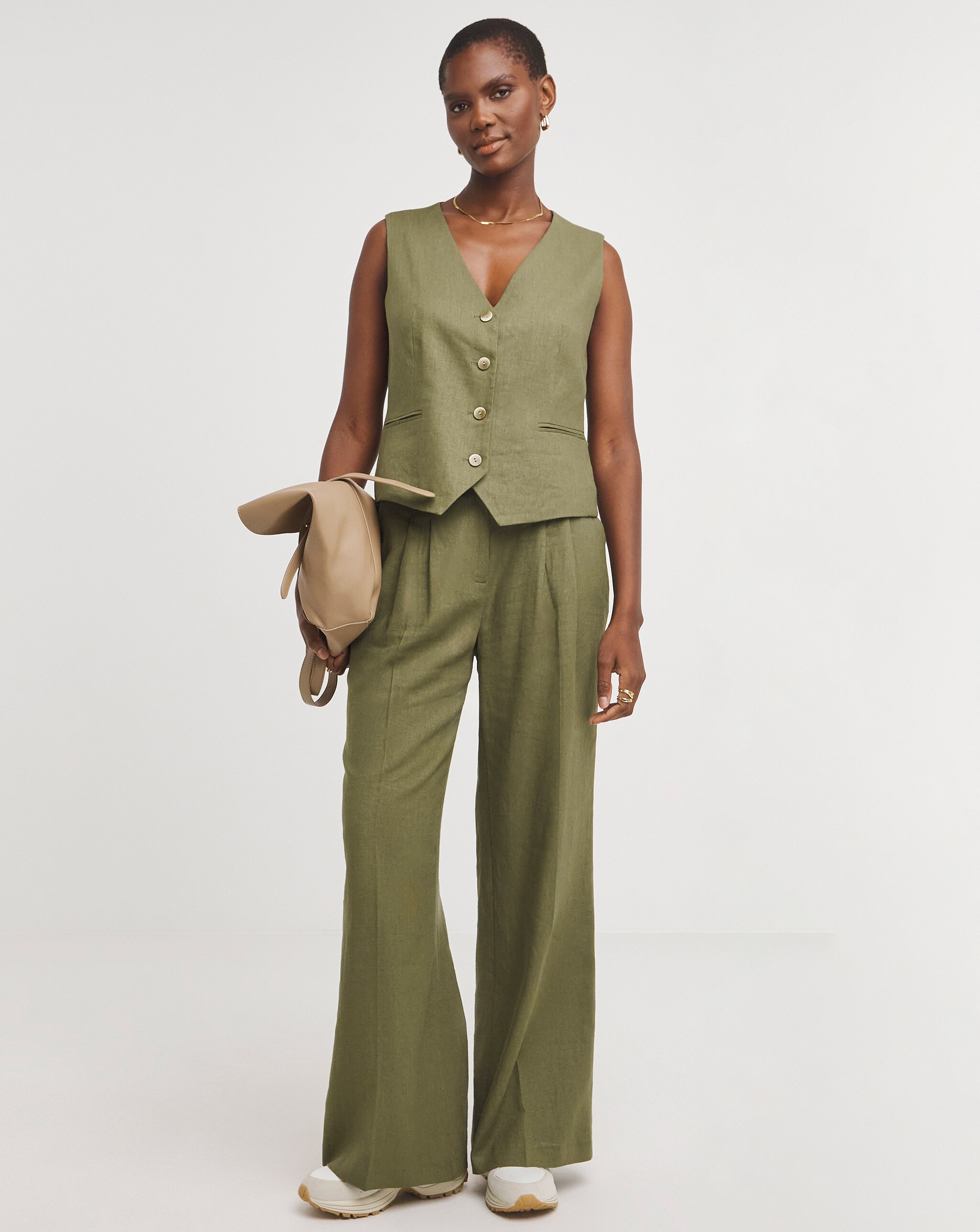 Person in an olive‑green sleeveless vest and matching wide‑leg trousers, holding a bag.