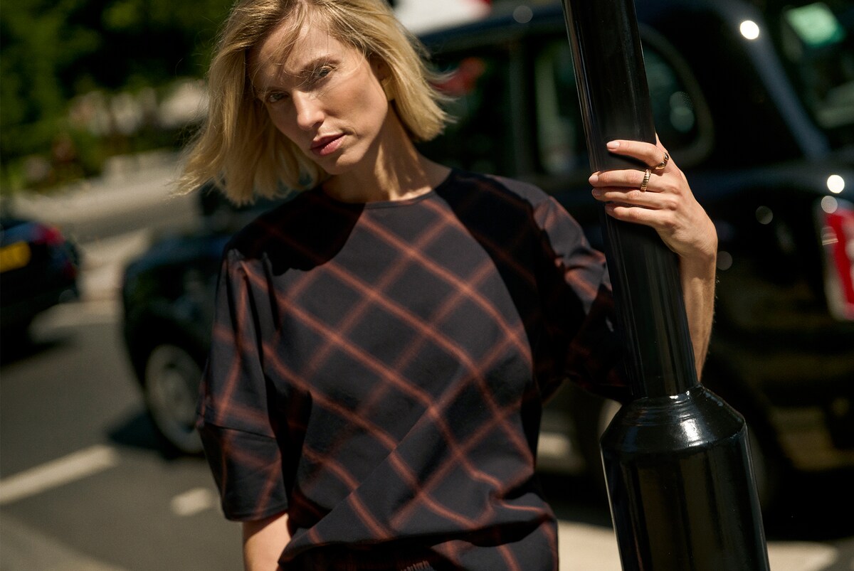 Person wearing a navy-coloured check-print top with puff sleeves, on a city street beside a black lamppost.
