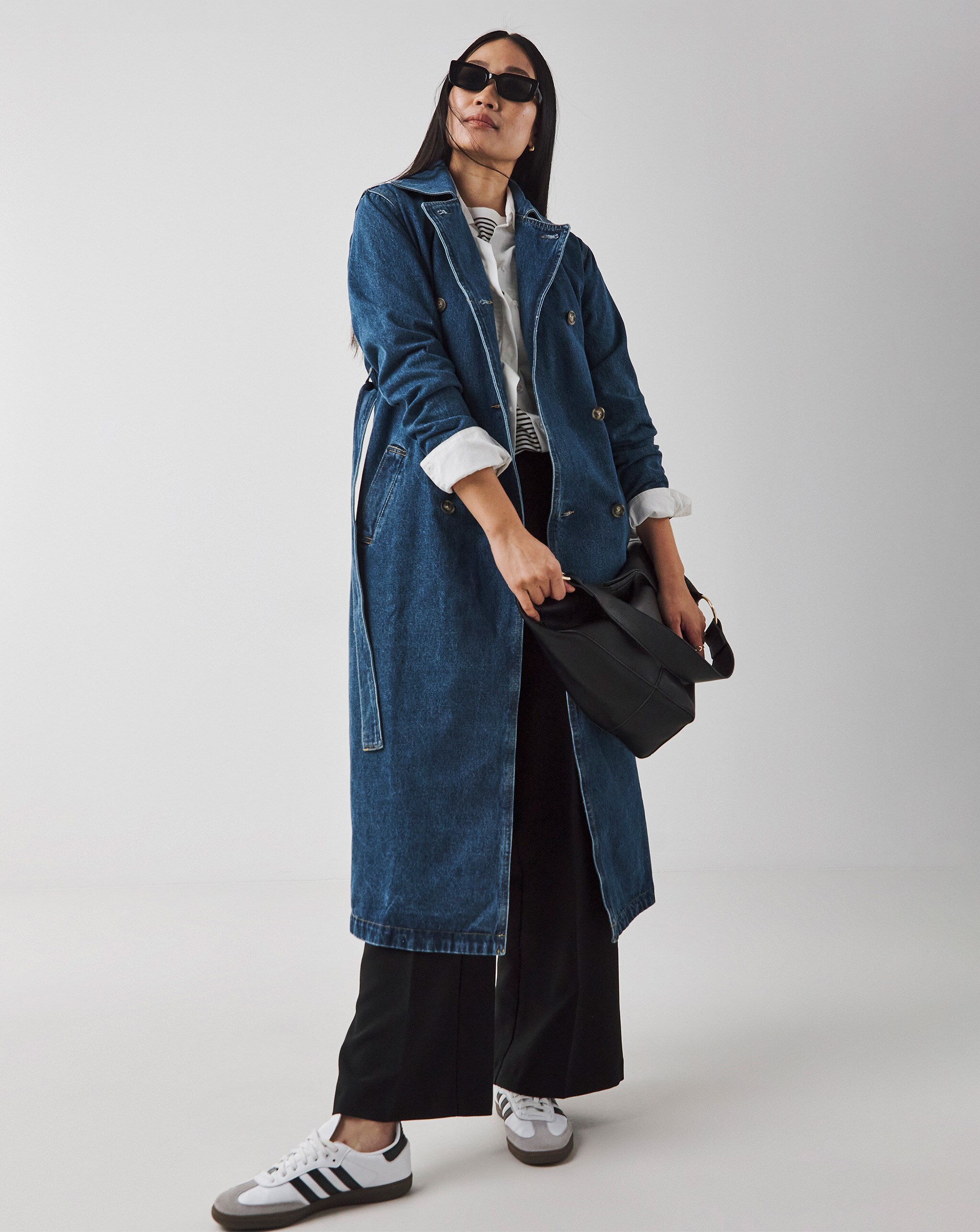 Person wearing a long dark denim trench coat over a striped top and black wide-leg trousers