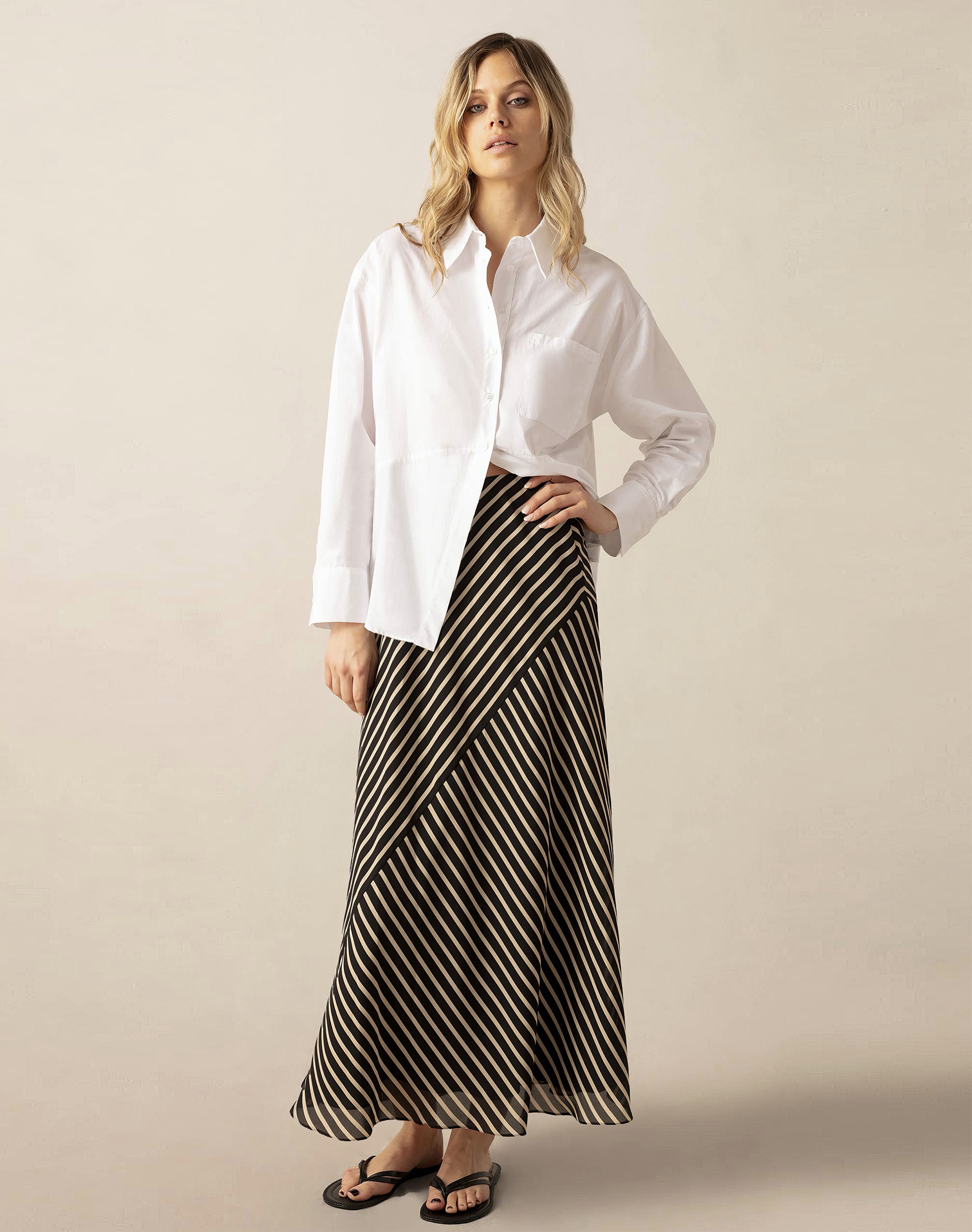A lady stood in front of a cream background wearing a stripey maxi skirt with a white blouse.