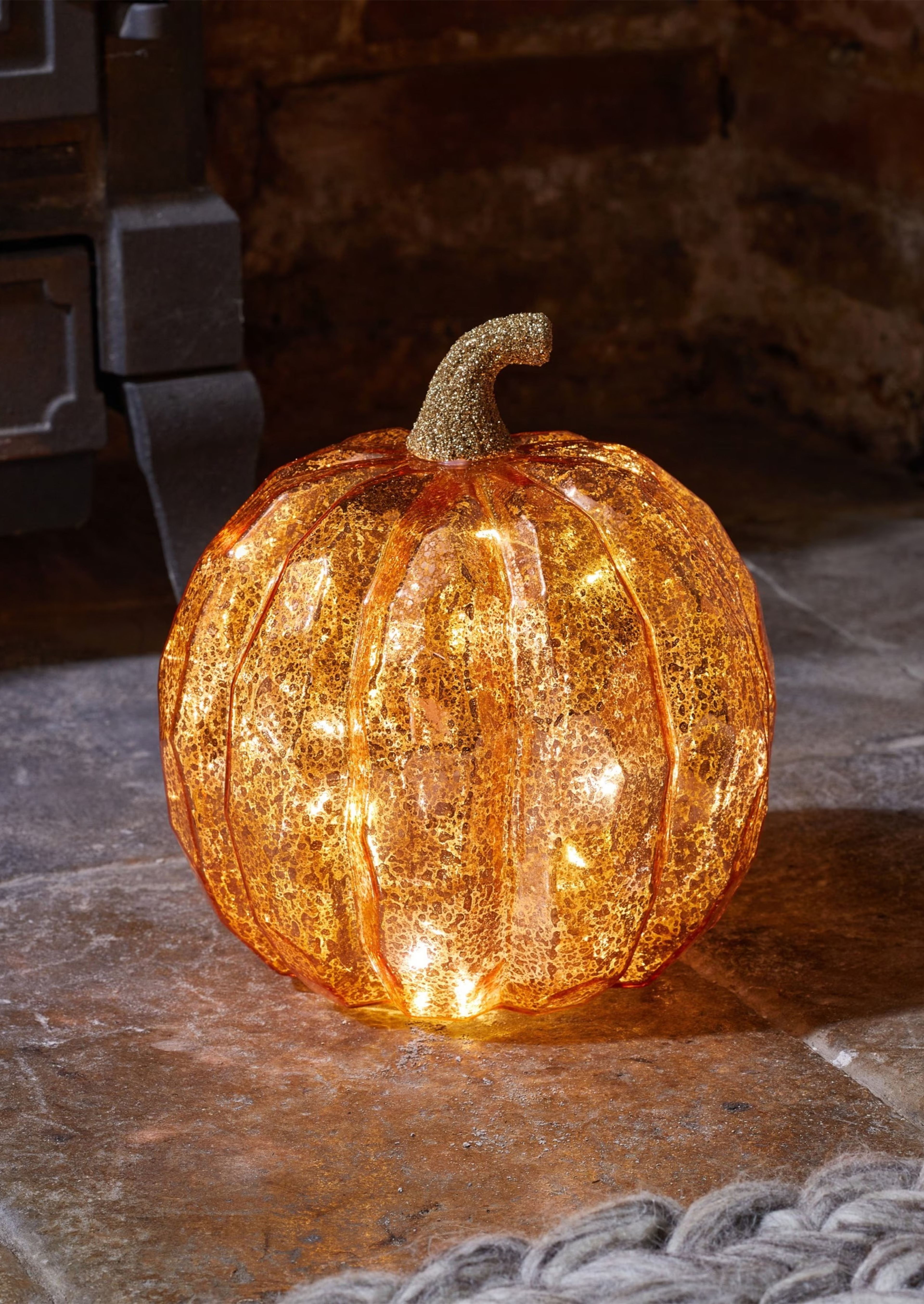 A led lit Halloween pumpkin ornament on a tiled floor next to a fire.