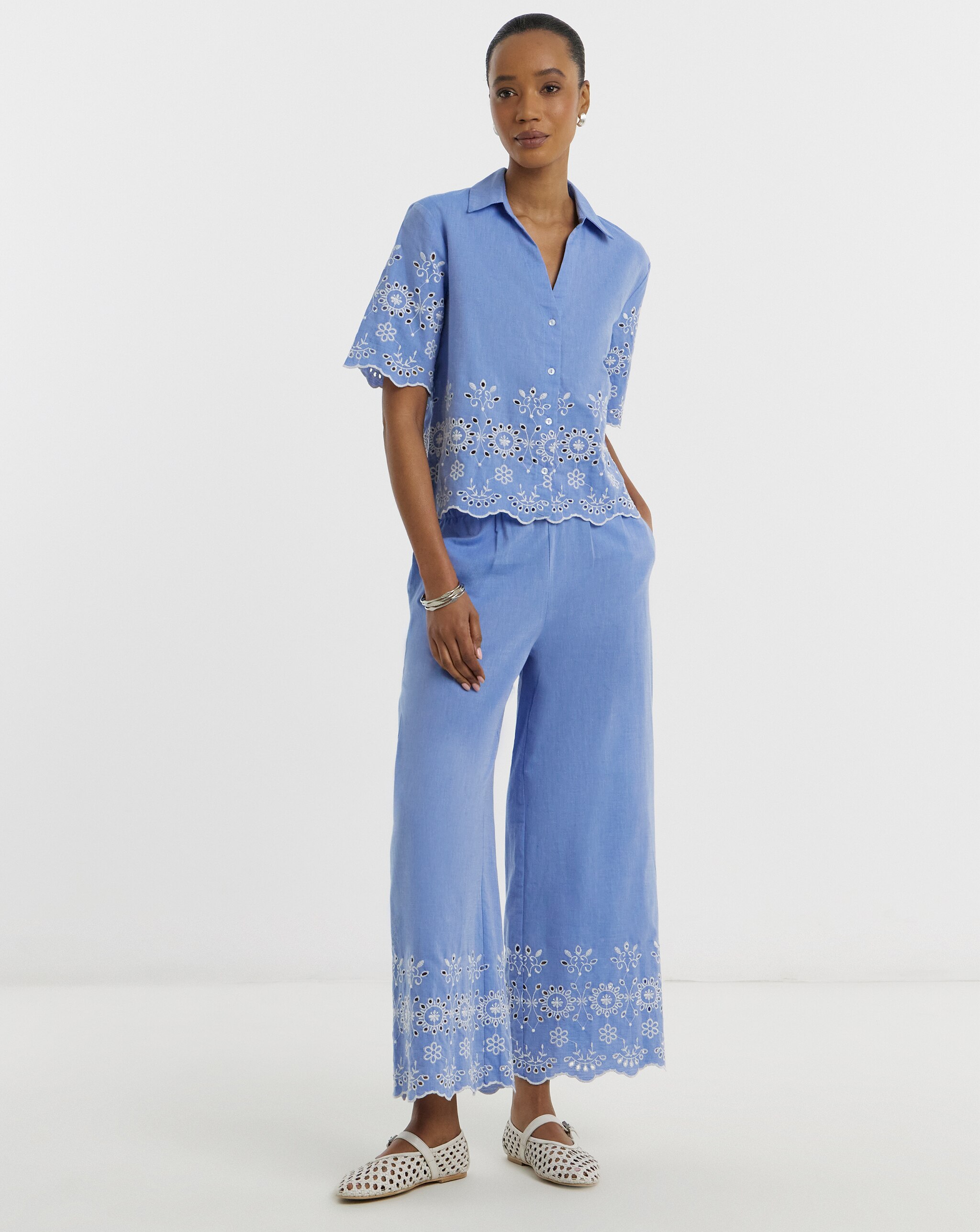 Person wearing a light blue embroidered short-sleeve shirt and wide-leg trousers with white woven flats.