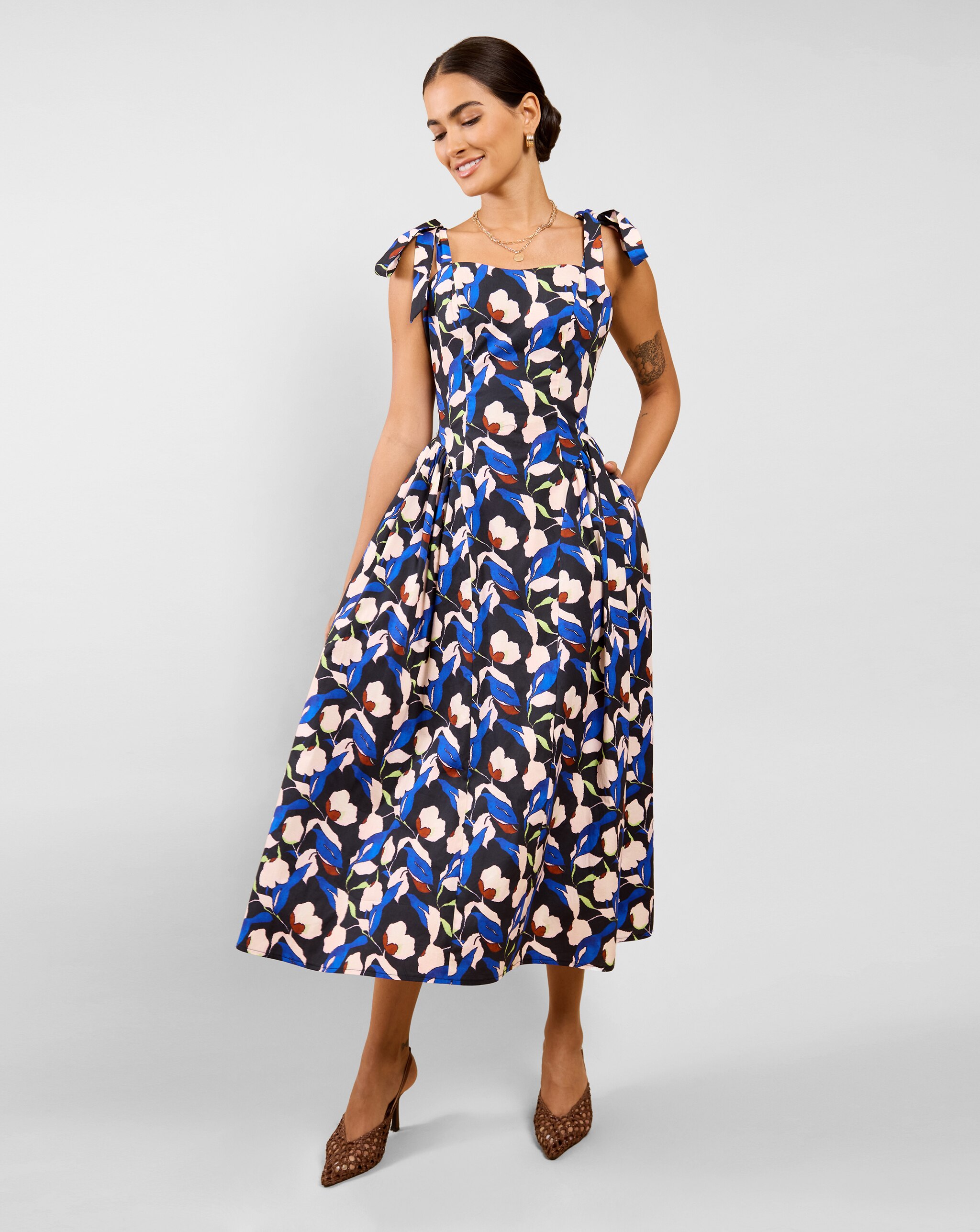 Person wearing a Little Mistress midi dress with a blue and cream floral print, tie-strap shoulders, and brown pointed heels.