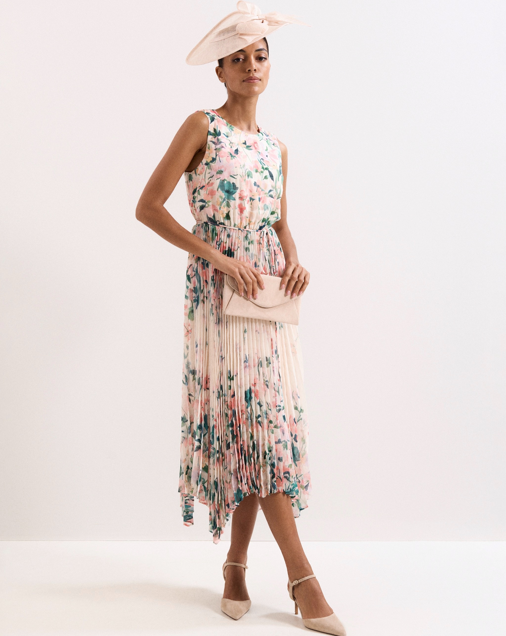Person wearing a blush floral pleated midi dress with nude heels, matching clutch bag, and a cream fascinator.
