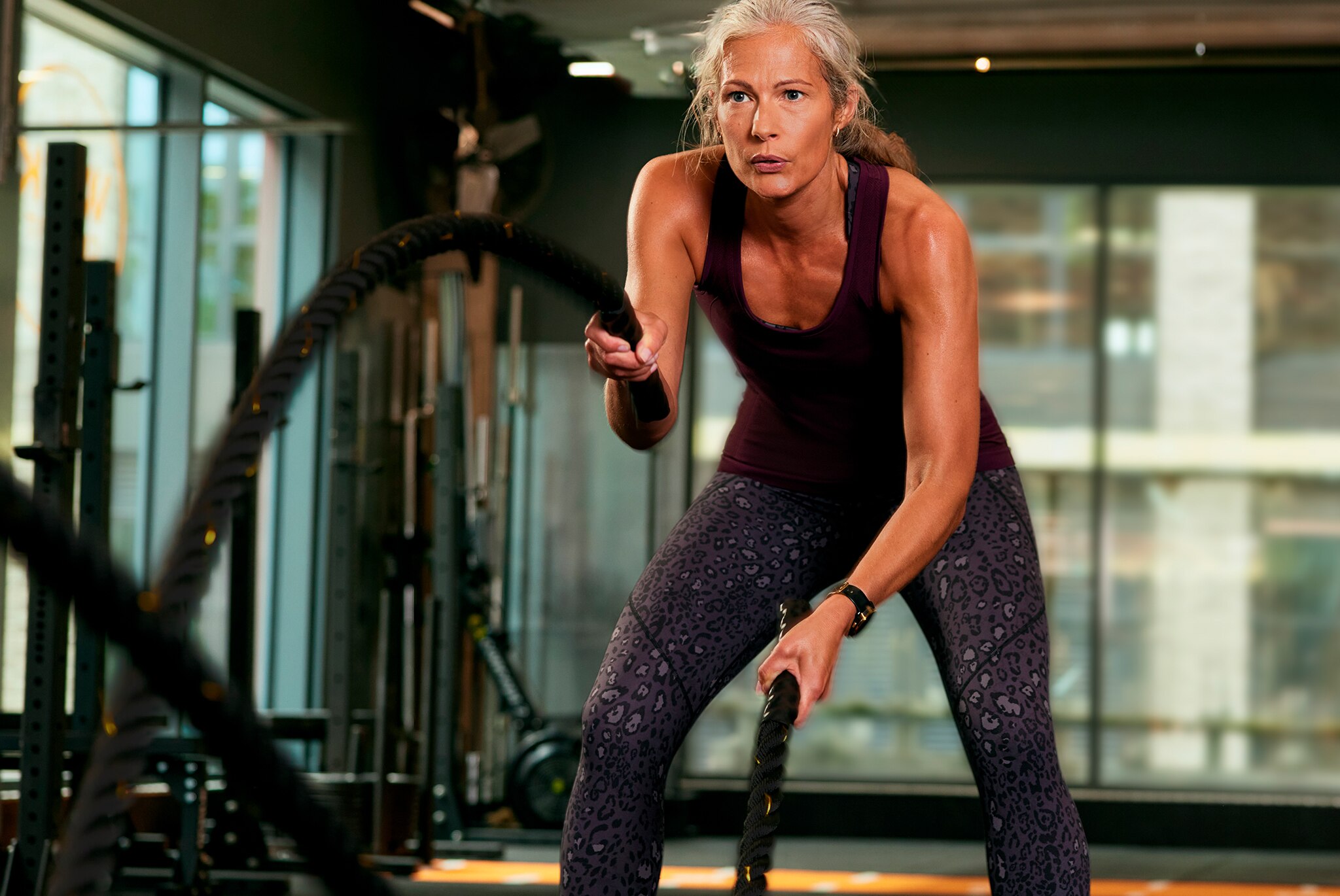 A woman wearing a black sports vest and grey leggings working out at a gym.