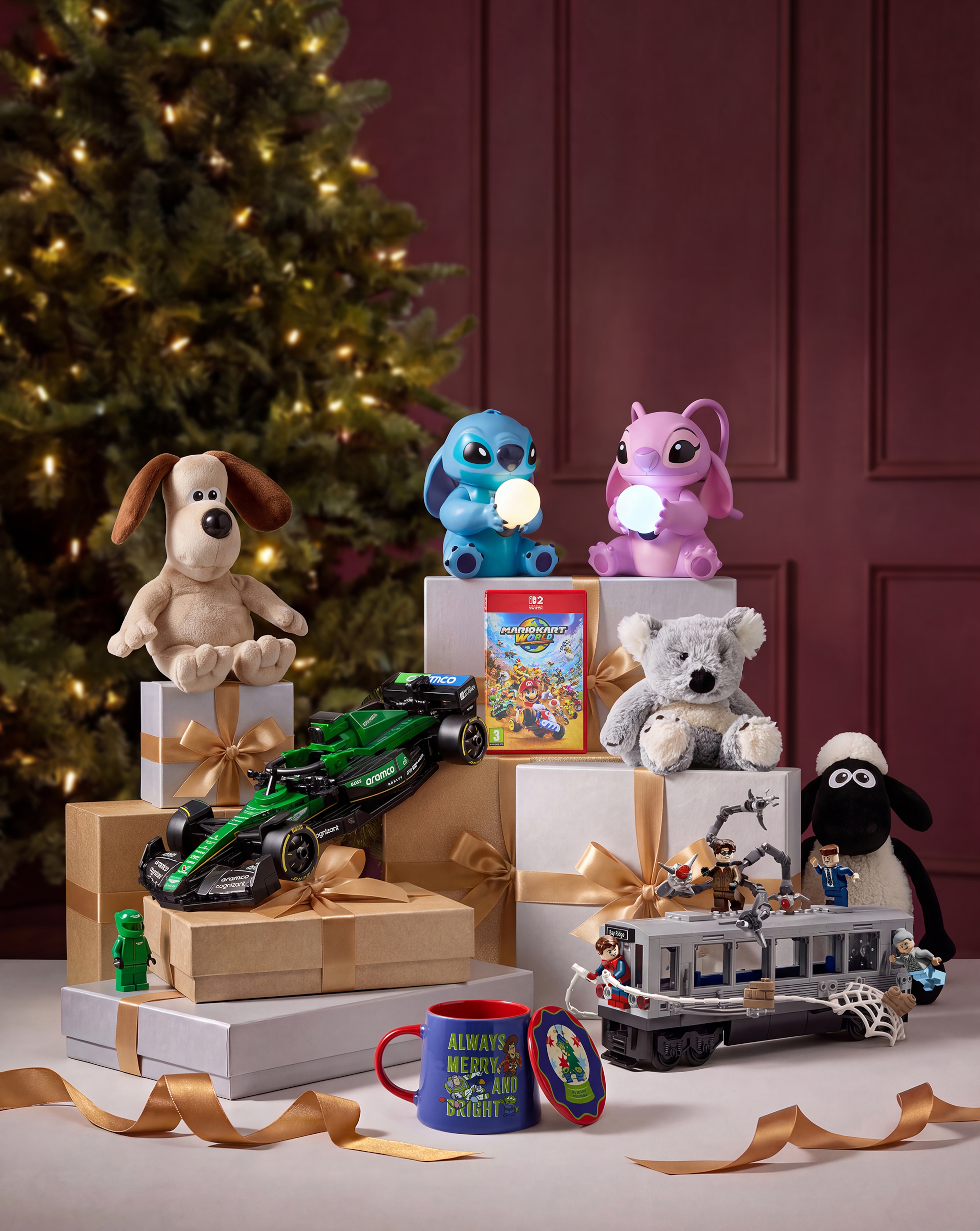 A collection of toys sat on and in between wrapped presents on a table with a Christmas tree in the background.