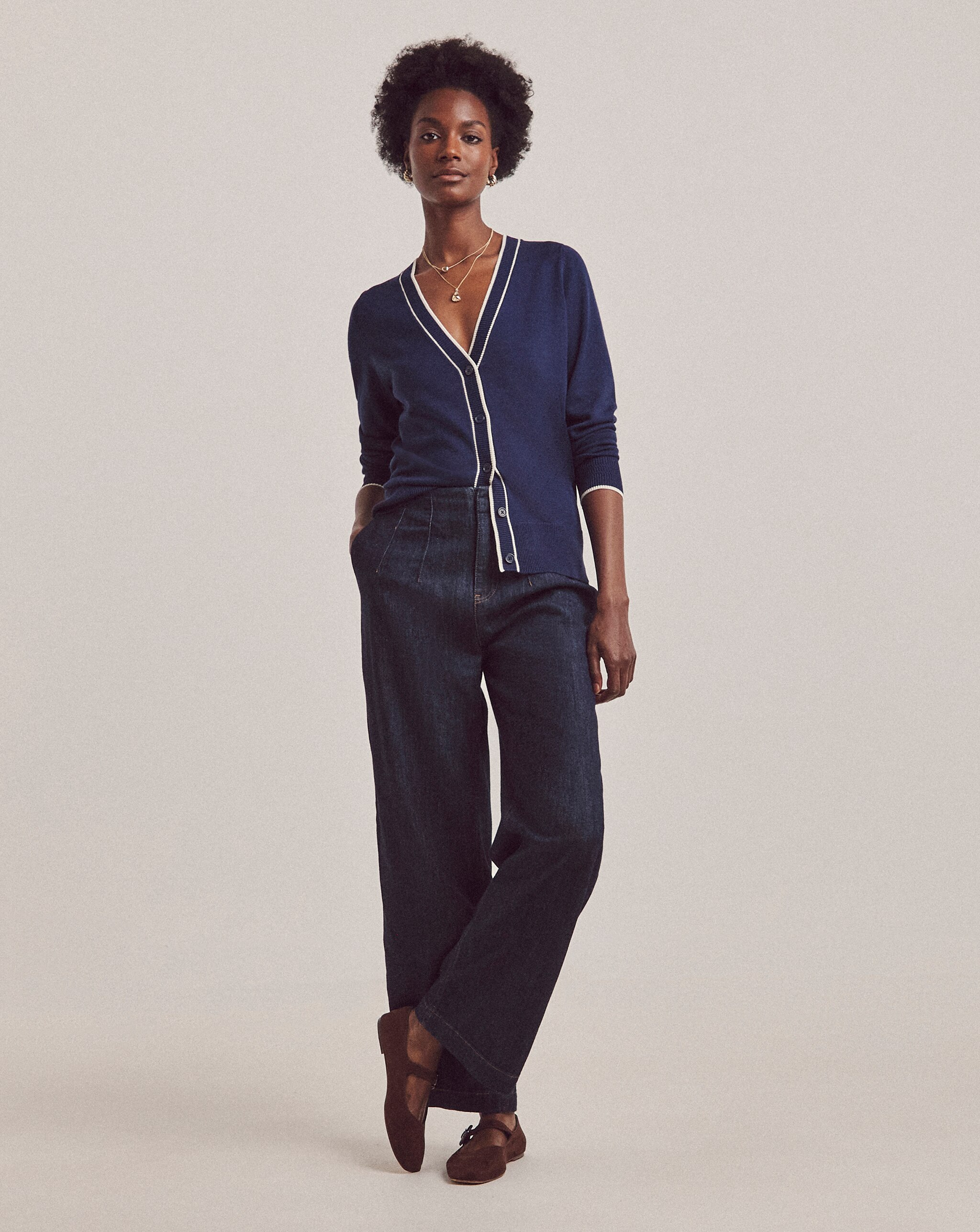 A woman wearing a blue cardigan with dark denim jeans.