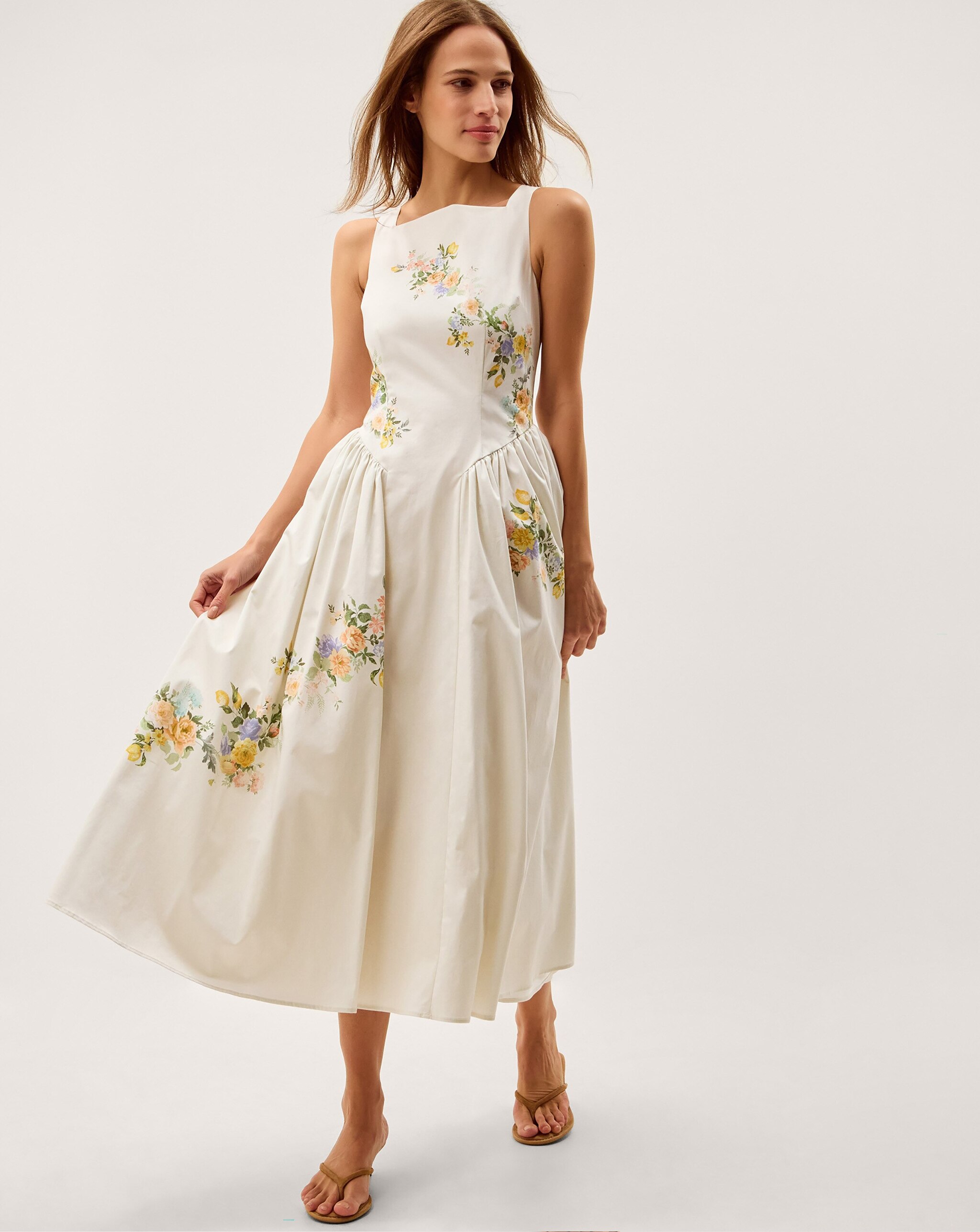 Person wearing a cream sleeveless midi dress with a pastel floral print and gathered skirt, styled with tan sandals.