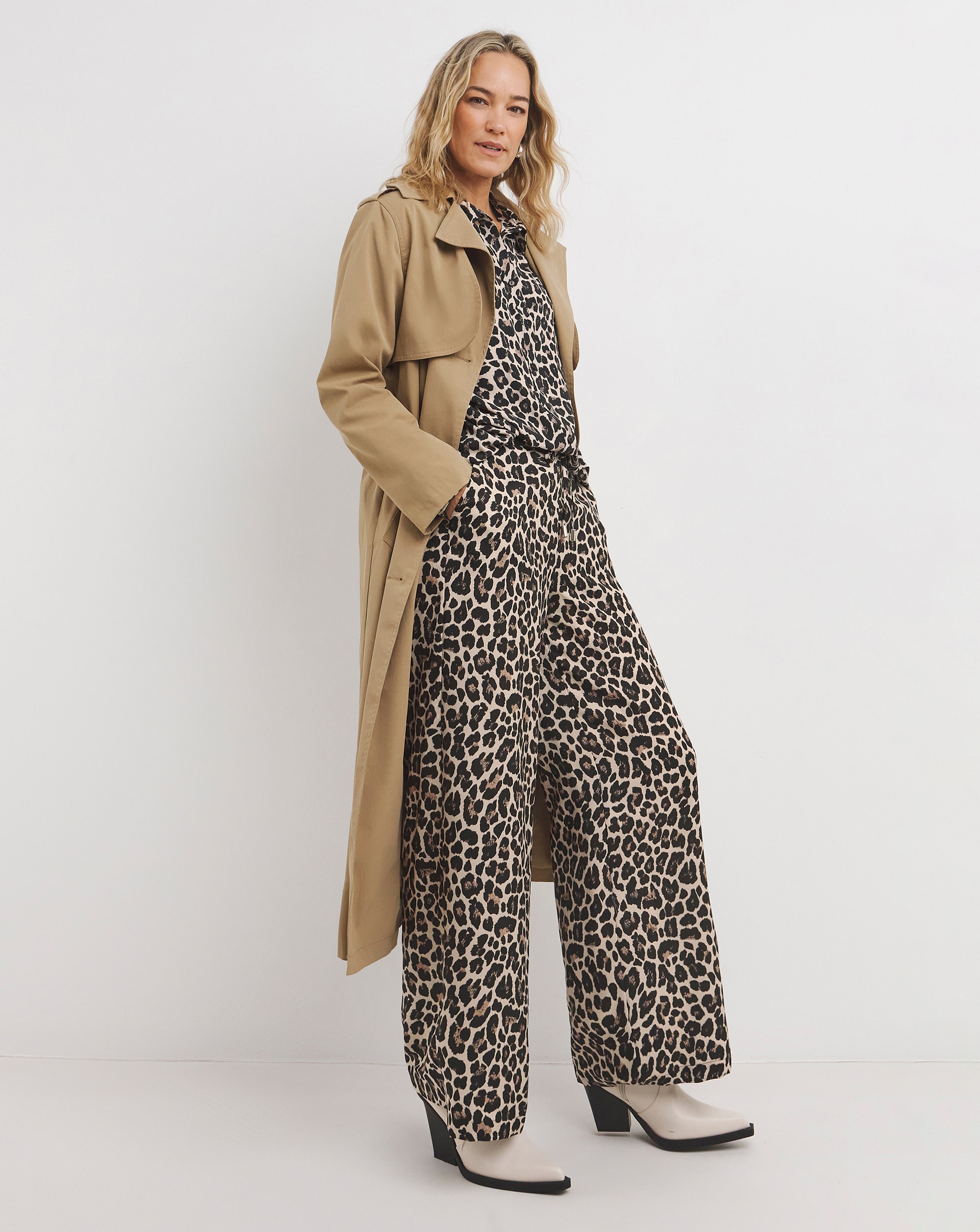 Person wearing a beige trench coat over a leopard-print matching set with black-and-white heeled boots.